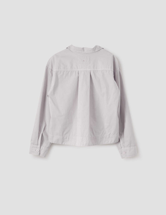 Beige boxy shirt with wide box pleat on back yoke and corozo brace buttons on cuffs. Back flat lay view.