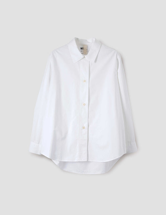 White long sleeve cotton shirt, with corozo button closure and cuffs and elongated hem. Front flat lay view.