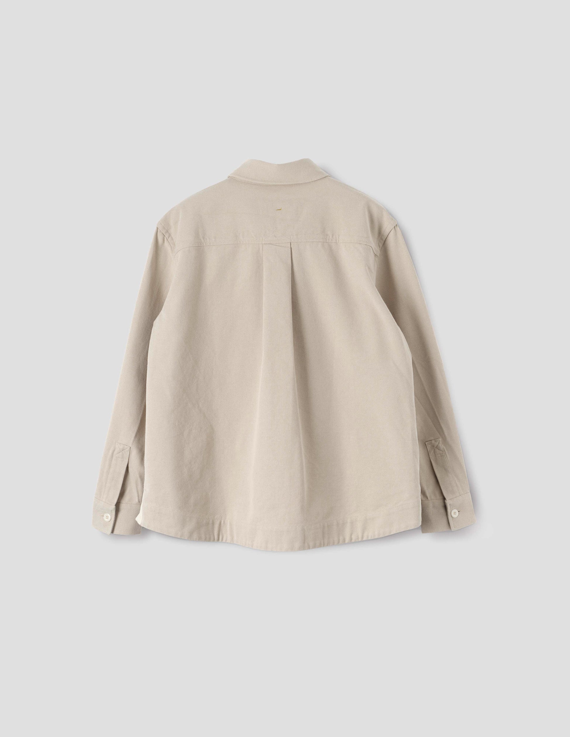 Beige oversized shirt with corozo button fastening cuffs, box pleat on back yoke and deep stitch hem. Back flat lay view. 