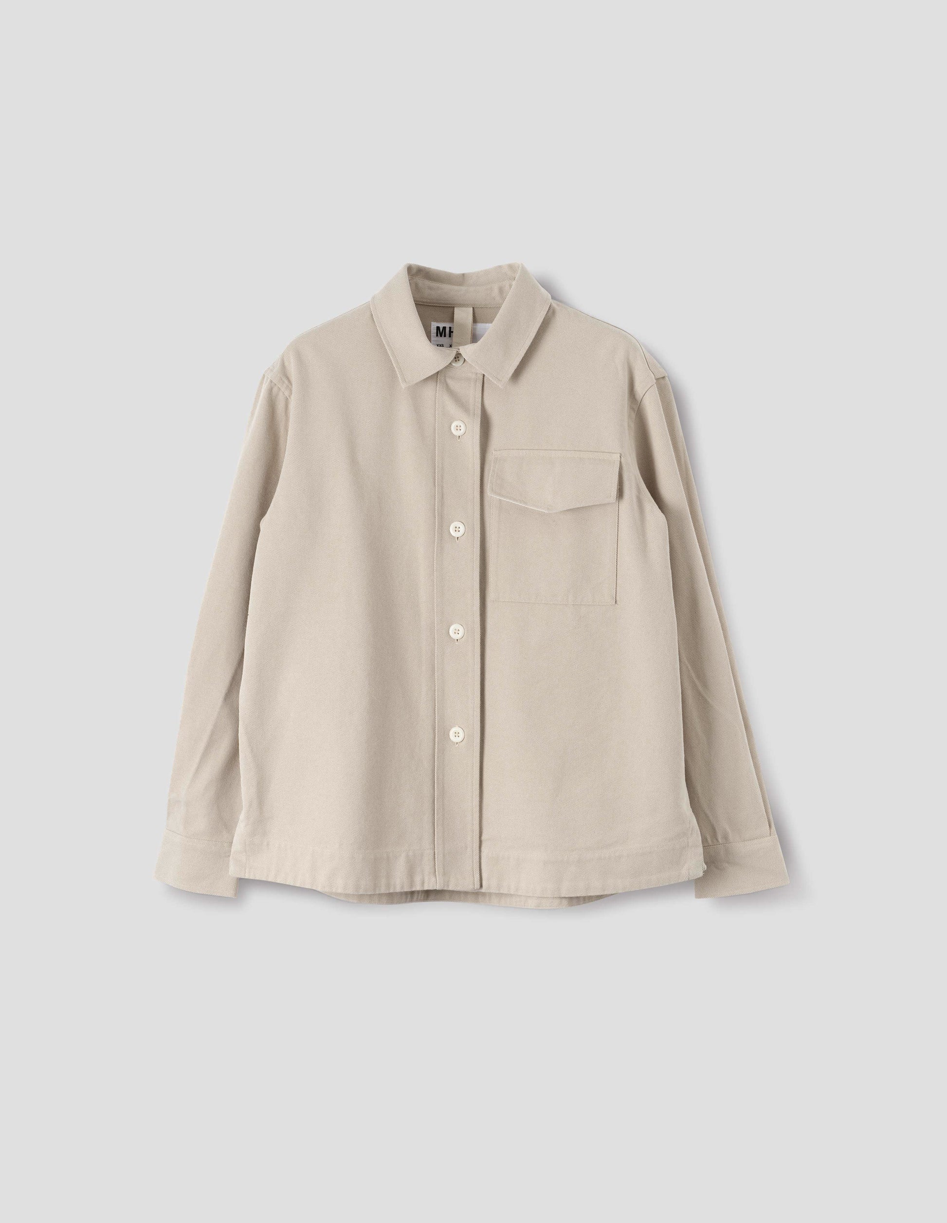 Beige oversized shirt with stitch through raised placket, corozo button fastening, patch chest pocket and deep stitch hem. Front flat lay view. 