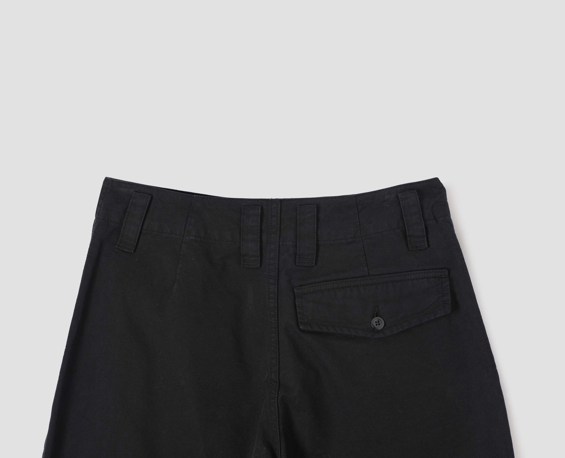 Black cotton canvas trousers with stitch-through waistband, dropped belt loops and button through flap back pocket. Back flat lay view.