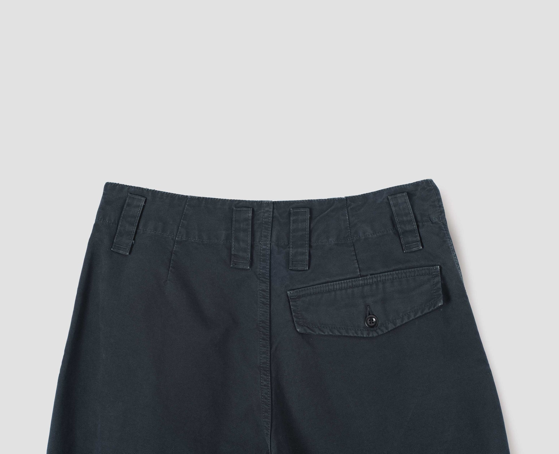 Blue cotton canvas trousers with stitch-through waistband, dropped belt loops and button through flap back pocket. Back flat lay view.