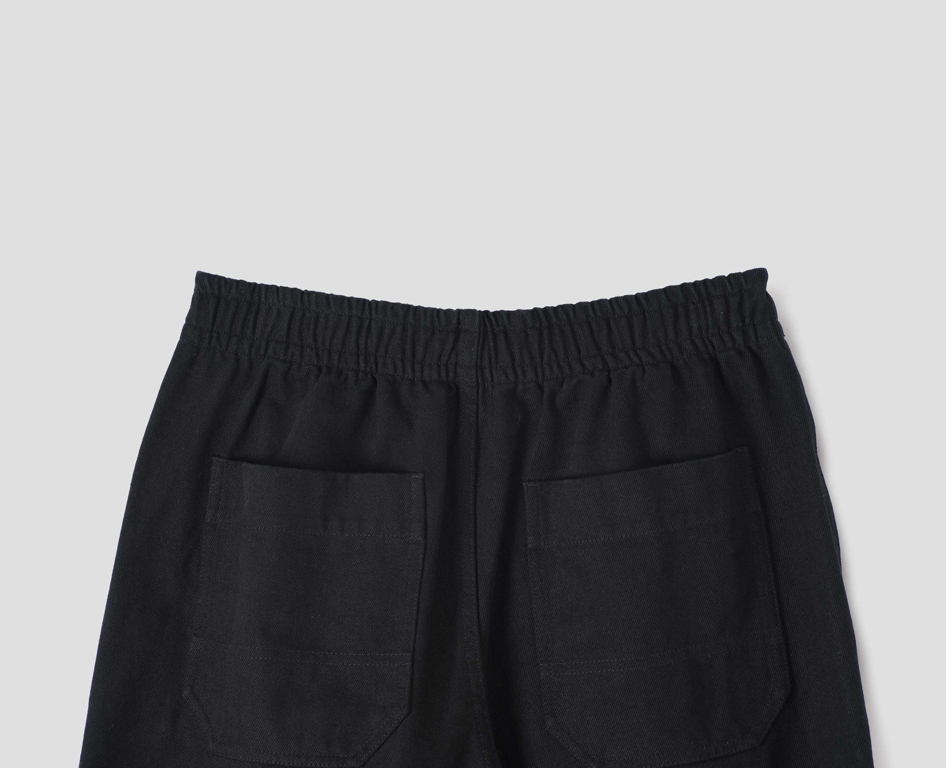 Black joggers with elasticated waistband and patch back pockets with reinforced stitch detailing, back flat lay view.