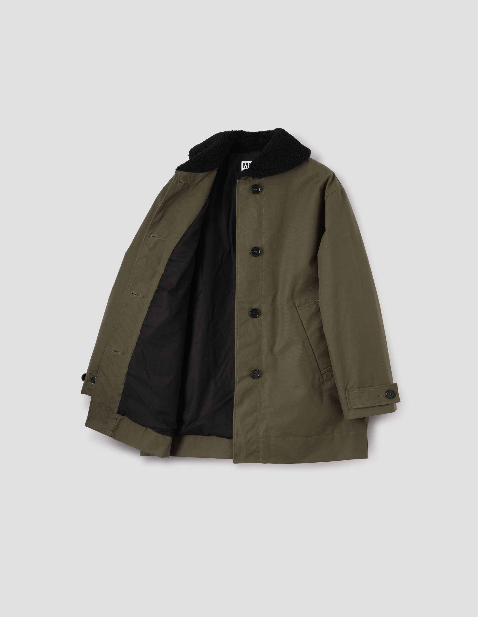 Khaki green coat with black fleece collar, slanted welt pockets with reinforced stitch detailing, corozo brace button fastening and button tab cuff adjusters, black padded lining. Open flat lay view.