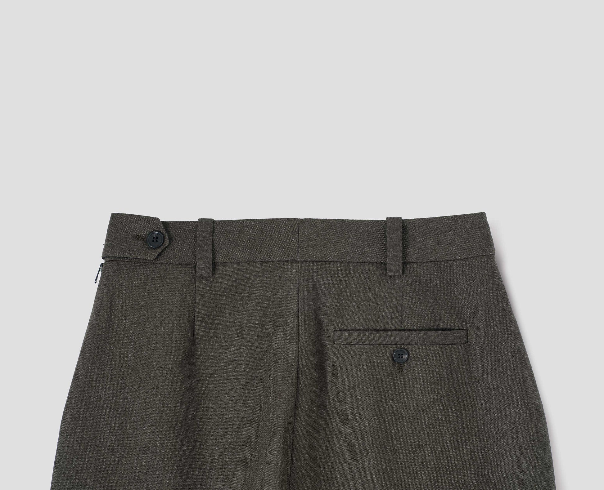 Brown trousers with belt loops and side zip, horn button tab waist fastening and welt button-through back pocket. Back flat lay view.