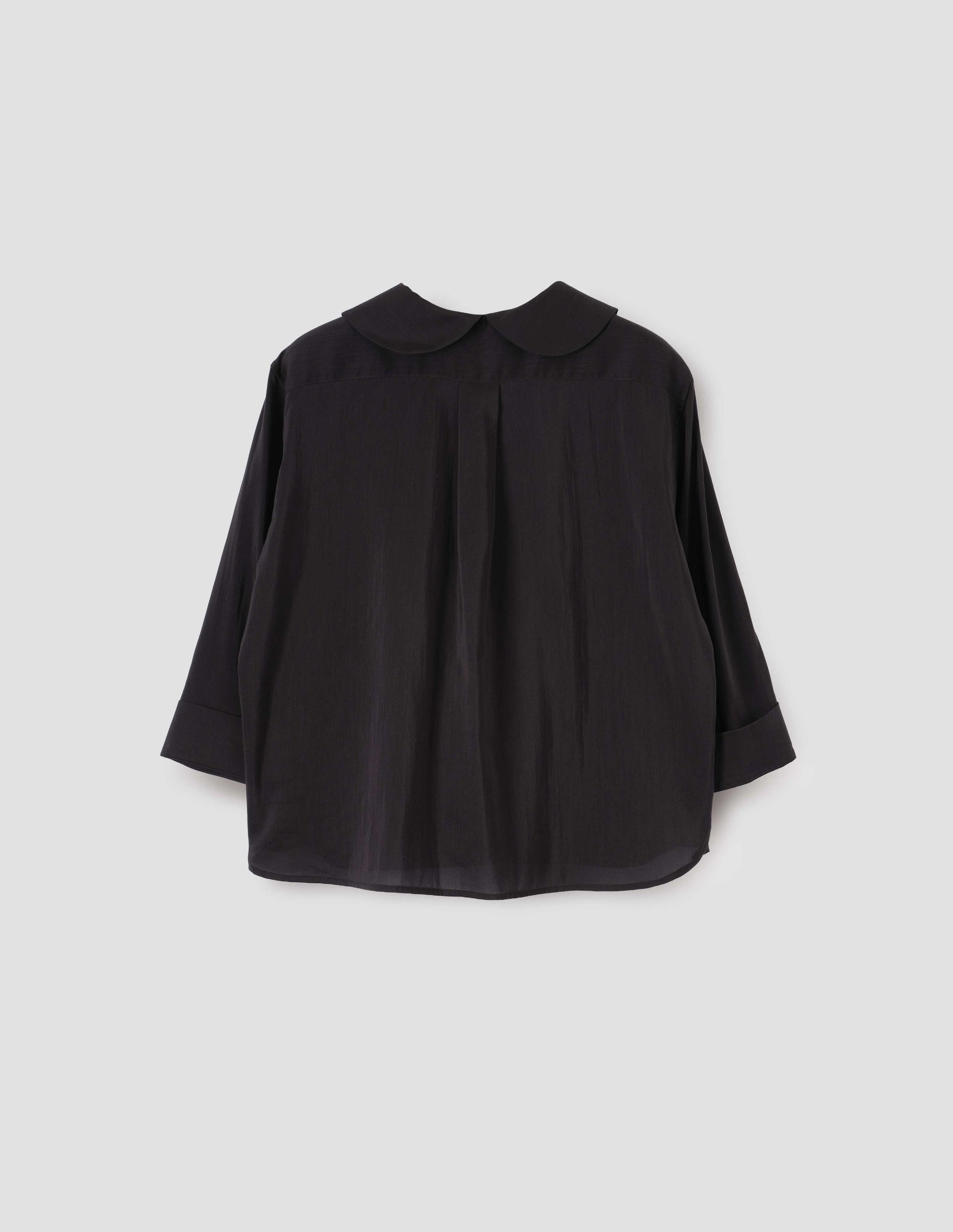 Black petal collar shirt with three quarter length sleeves, turned back cuff details and box pleat on back yoke. Back flat lay view.