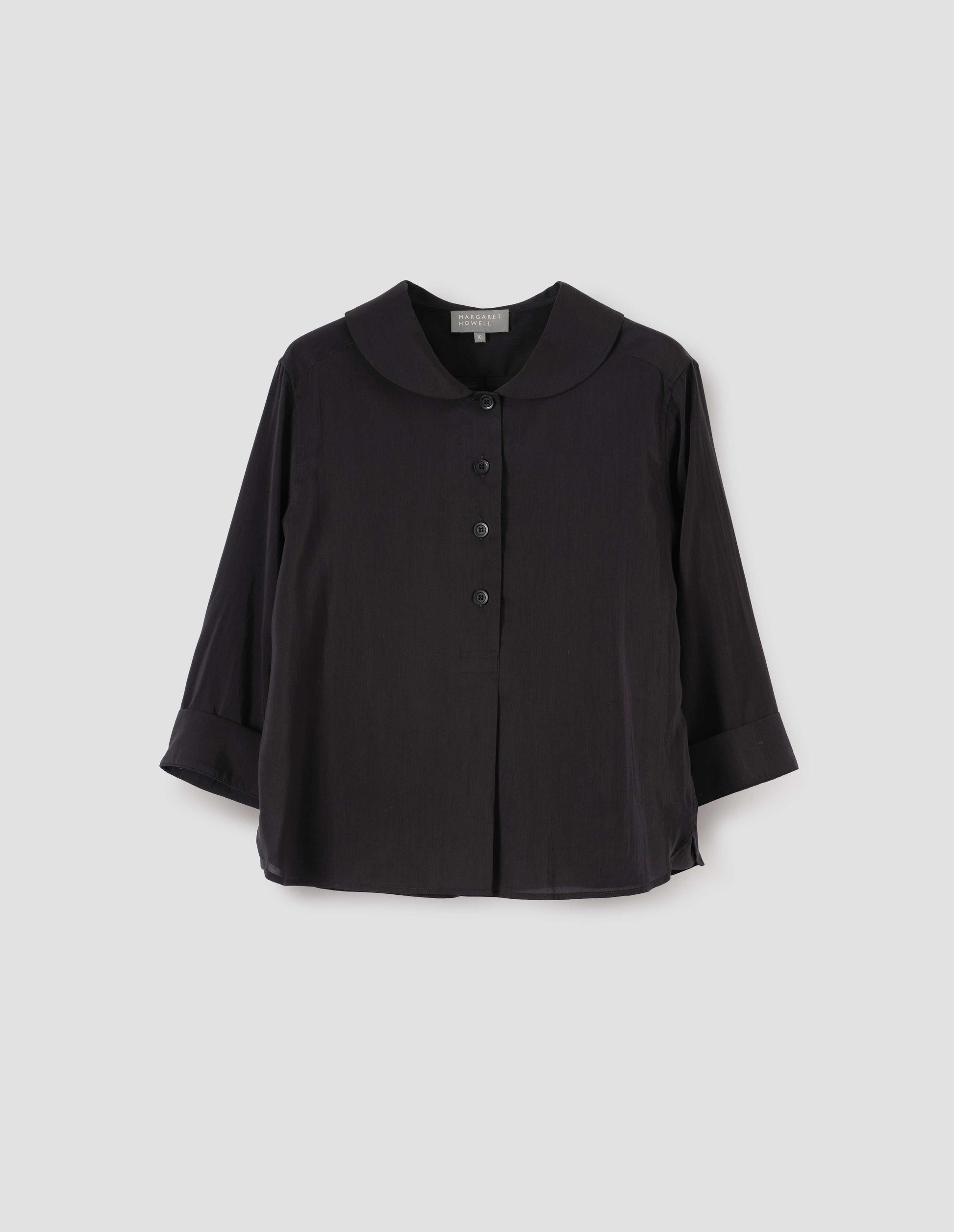 Black petal collar shirt with three quarter length sleeves, stitch through half placket, mother of pearl buttons and turned back cuff details. Front flat lay view.