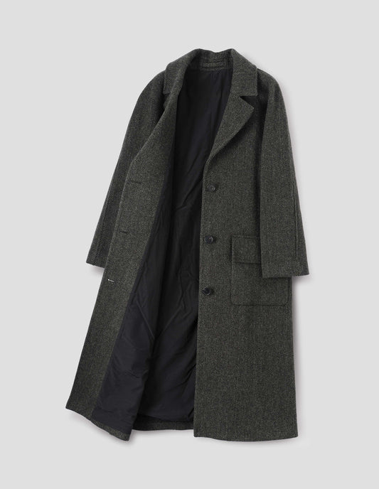 Green and black herringbone wool longline overcoat with raglan sleeve, button fastening lapel and deep flap patch pockets and fully lined in black cotton. Front flat lay open view.