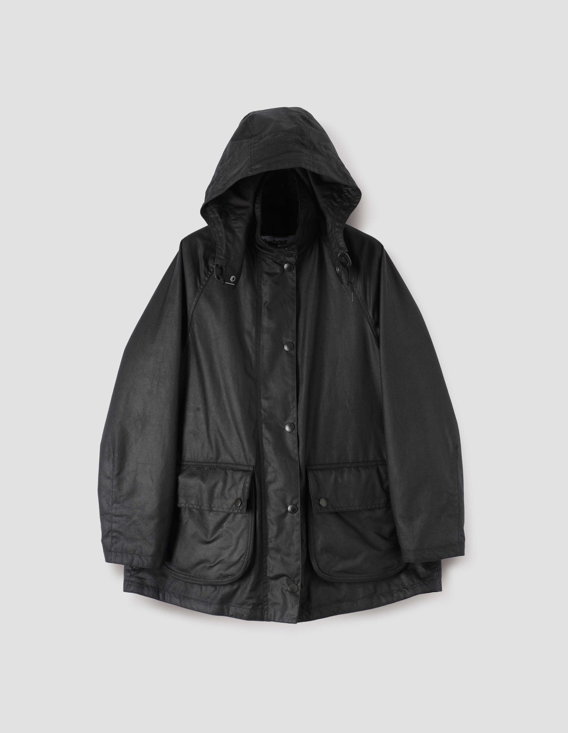 Black parka with stand collar and hood with wire adjustable peak, raglan sleeve, press stud fastening storm flap and large bellows pockets with press stud fastening envelope closure. Front flat lay view.
