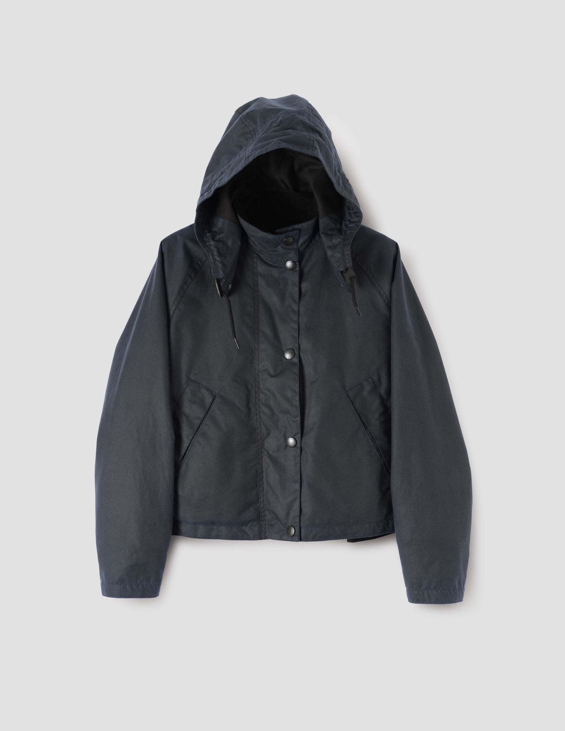 Dark blue boxy jacket with stand collar and hood with wire adjustable peak, raglan sleeve, press stud storm flap and wide storm welt side pockets. Front flat lay view.