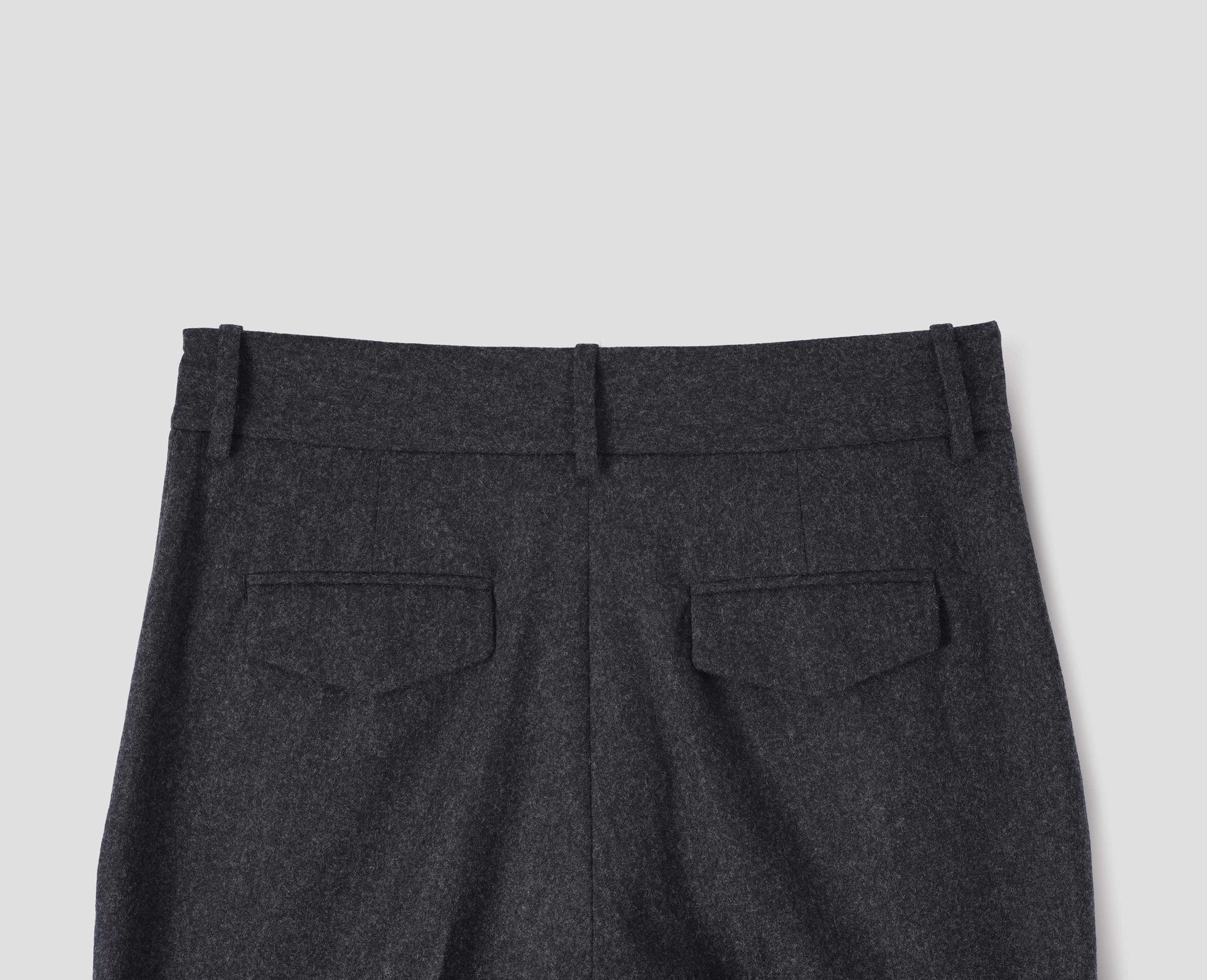 Charcoal grey wool trousers with slant side pockets, belt loops and flap back concealed pockets. Back flat lay view.