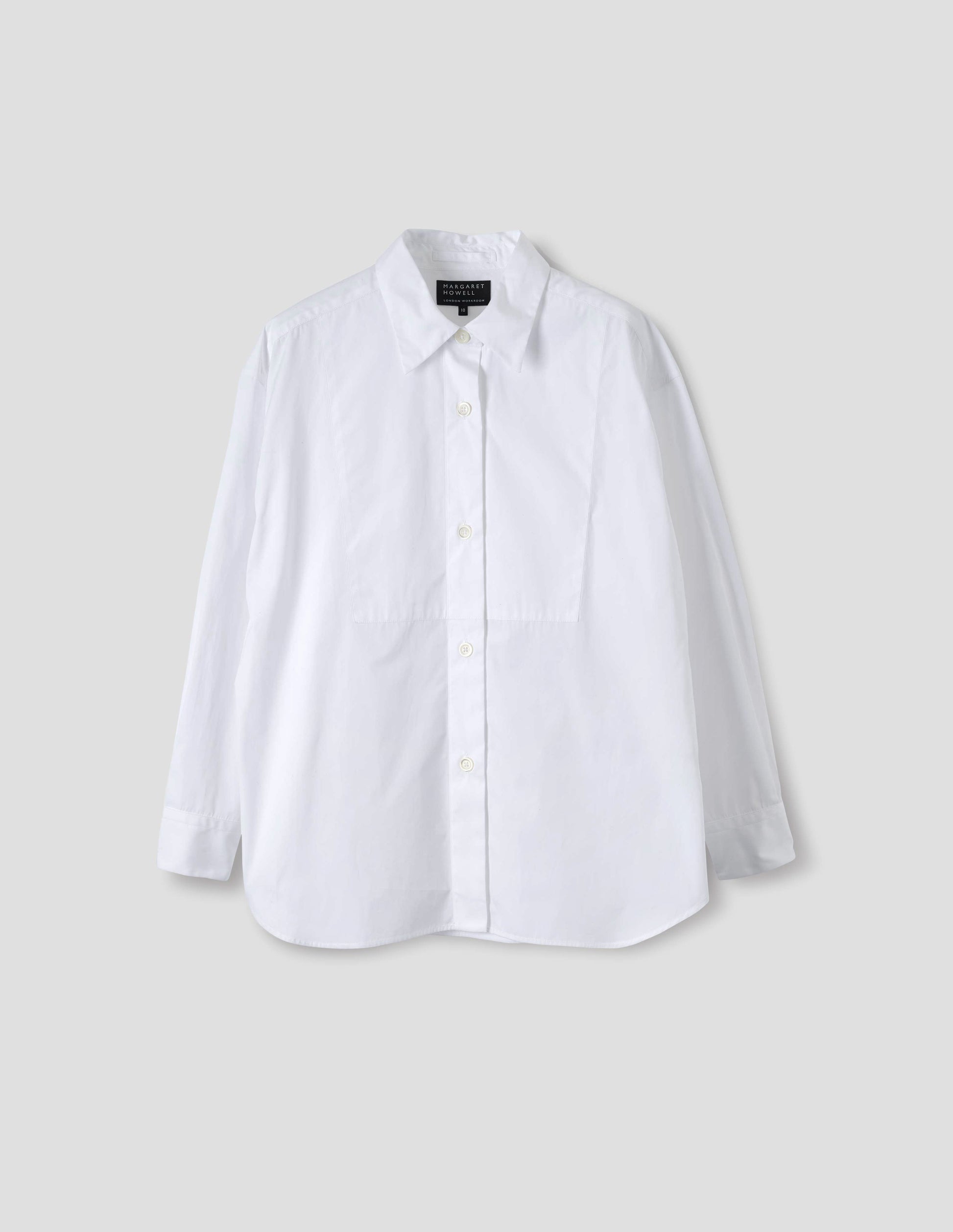 White cotton shirt with pointed stand collar, mother of pearl buttons on placket, double-layer bib front and curved hem. Front flat lay view.