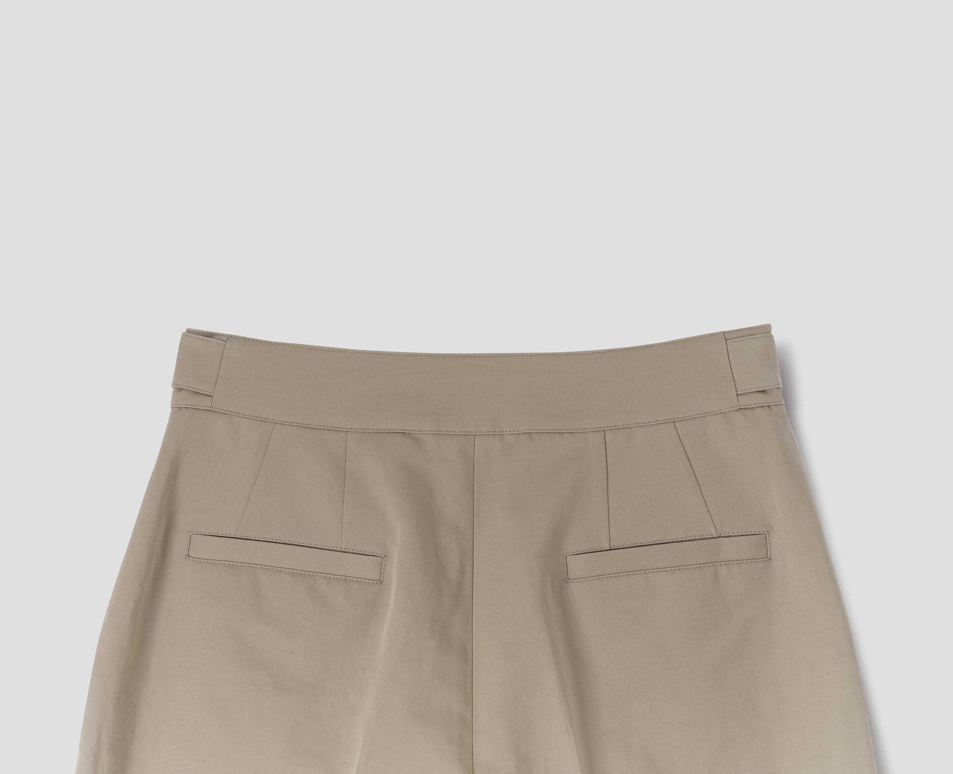 Beige cotton linen trousers with side cinches and welt back pockets. Back flat lay view.