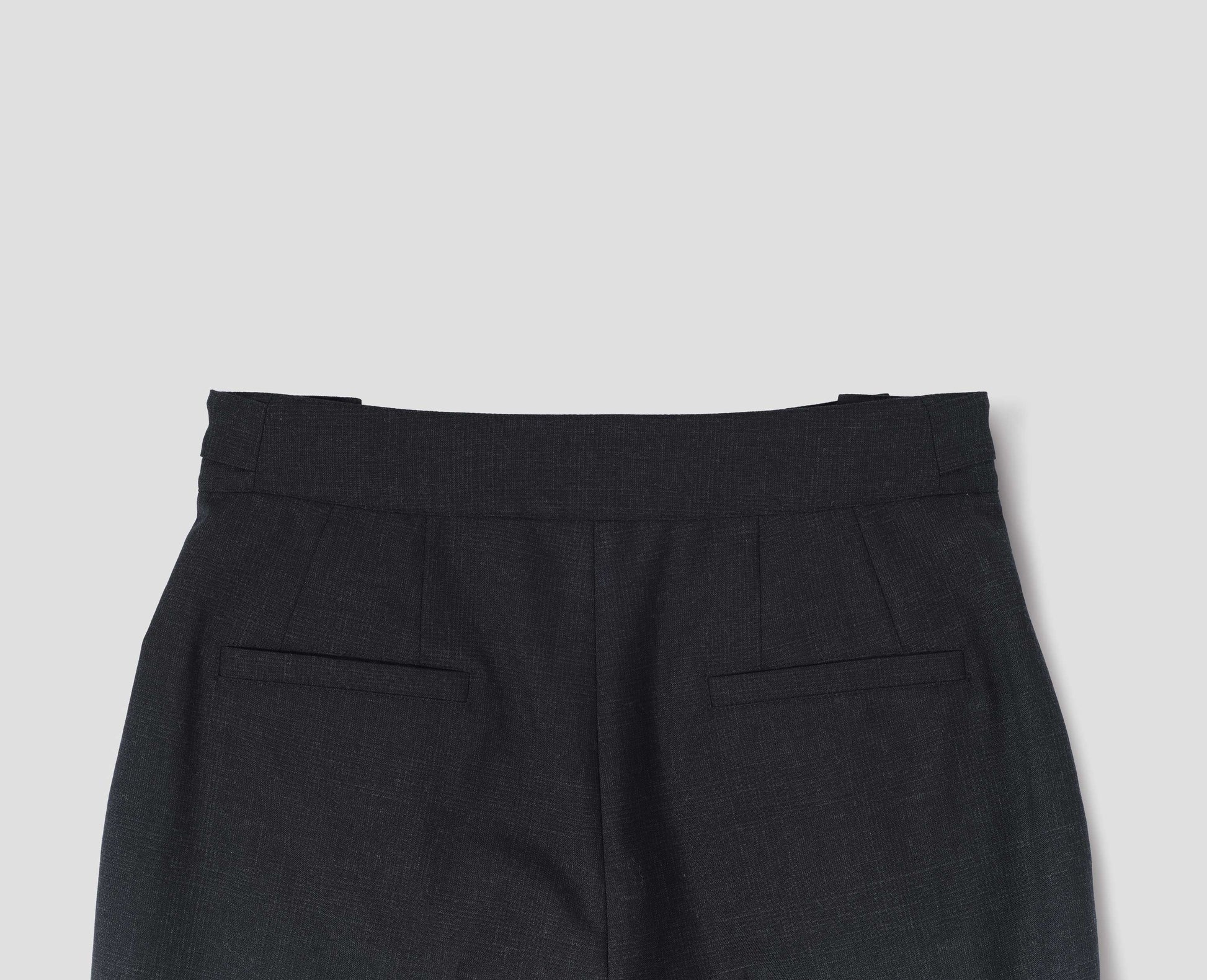 Dark grey wool trousers with side cinches and welt back pockets. Back flat lay view.
