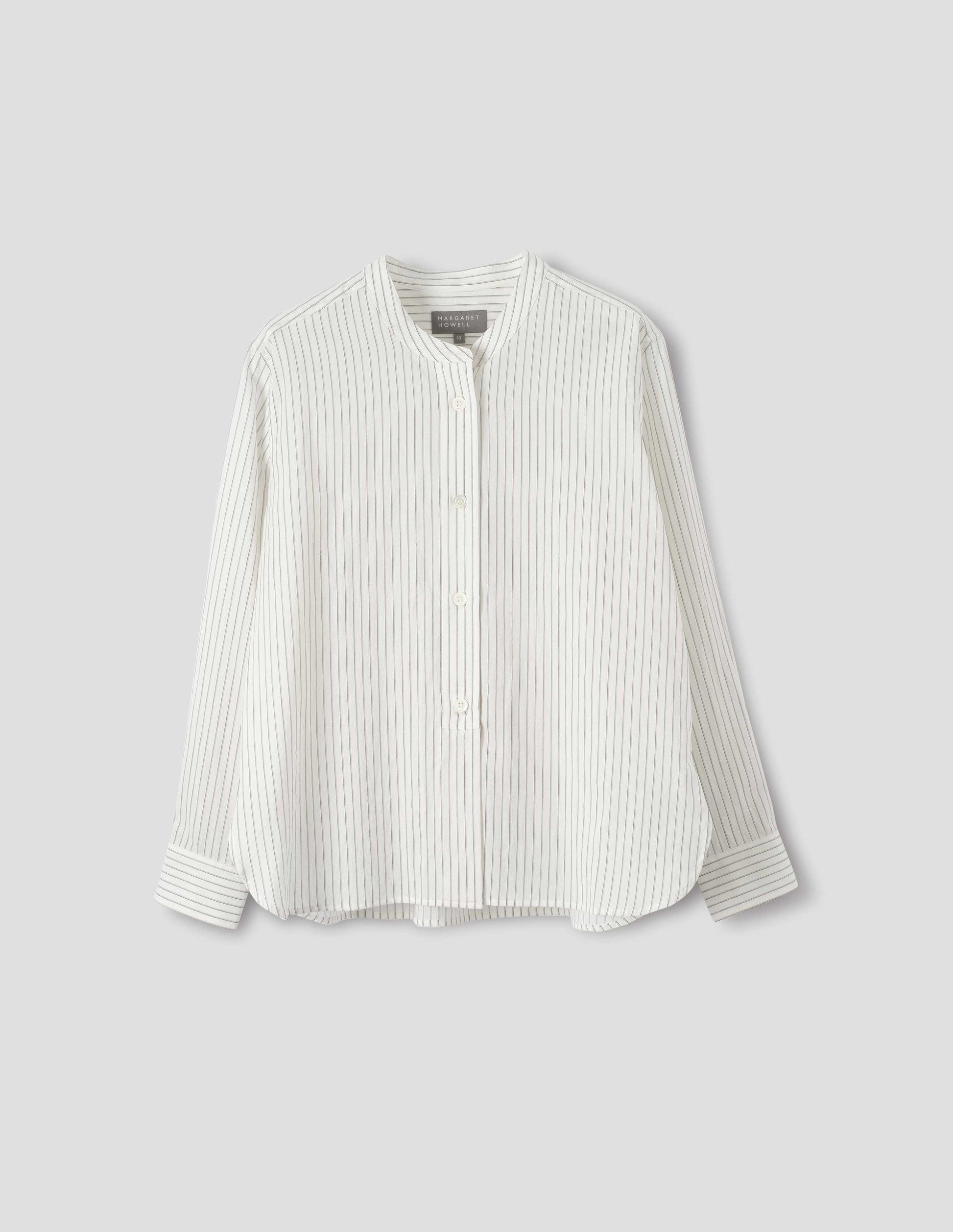 White collarless cotton and silk shirt with grey stripes, mother of pearl buttons on raised placket with box stitch detailing and curved hem. Front flat lay view.