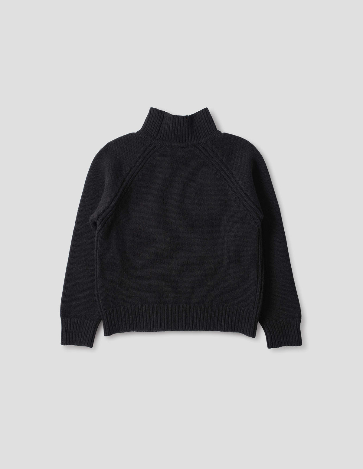 Black merino jumper with plain knitted back, raglan sleeves with ribbed side seams and ribbed high neck collar, cuffs and hem. Back flat lay view.