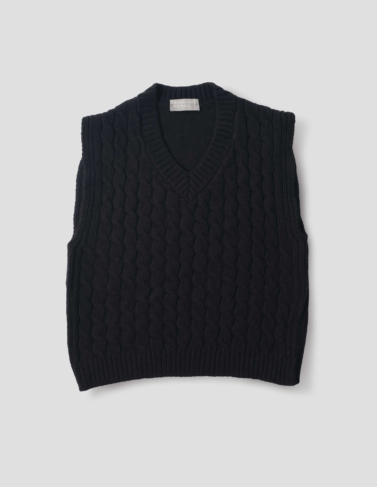 Black wool slipover with V neck, front cable design and ribbed neck, armholes, side seams and hem. Front flat lay view.
