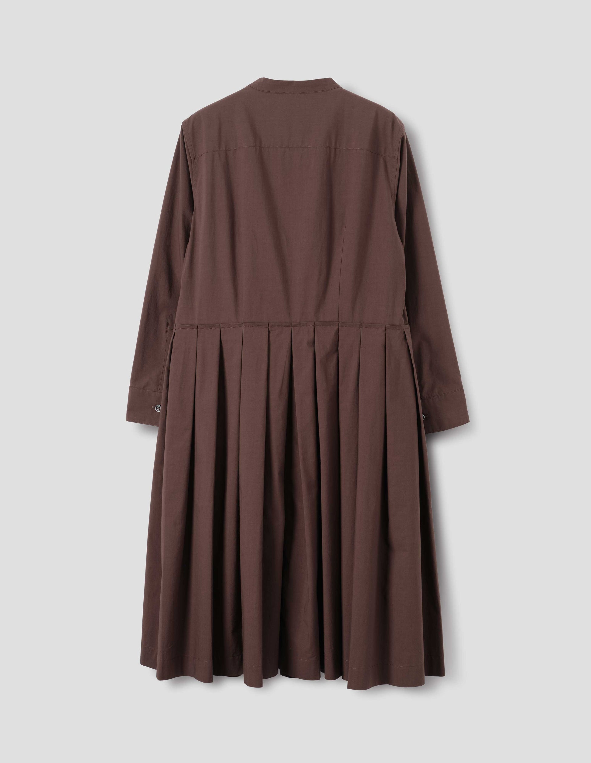 Brown collarless cotton dress with shirt yoke, long sleeves with mother of pearl buttons on cuffs and pleated skirt with concealed side pockets. Back flat lay view.