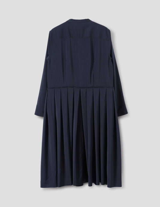 Dark blue collarless wool dress with shirt yoke, long sleeves with mother of pearl buttons on cuffs and pleated skirt with concealed side pockets. Back flat lay view.