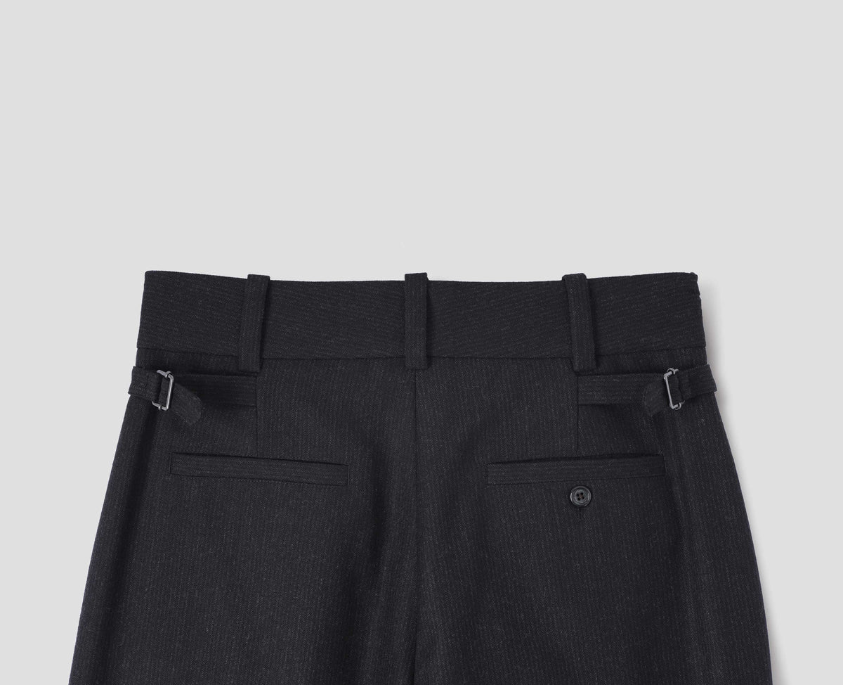 Black wool trousers with dark grey stripes, belt loops on wide waistband, side adjusters and two welt back pockets, one with horn button fastening. Back flat lay view.
