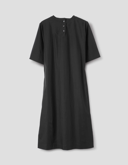 Black cotton blend dress with bias cut binding neckline, three mother of pearl buttons at centre, deep hem sleeves, side seam pockets and deep vent split hem. Back flat lay view.