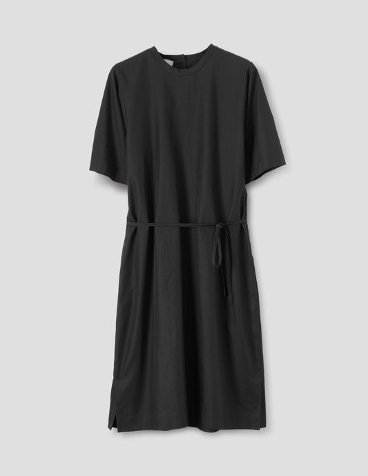 Black cotton blend dress with bias cut binding neckline, deep hem sleeves, thin belt in self fabric, side seam pockets, and deep vent split hem. Front flat lay view.