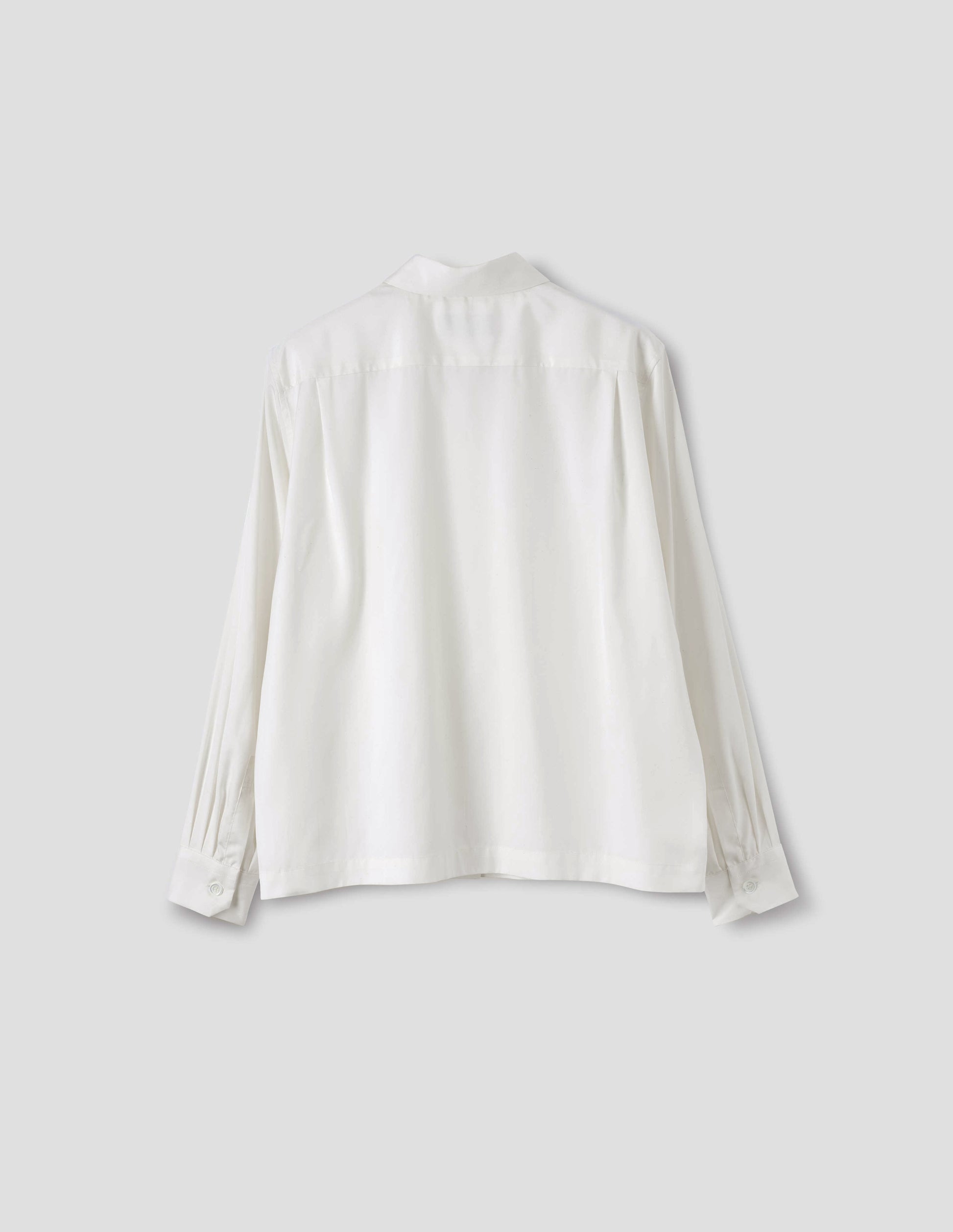 White silk shirt with narrow shoulder yoke with two pleats, mother of pearl buttons on angled cuffs, and with vent split hem. Back flat lay view.