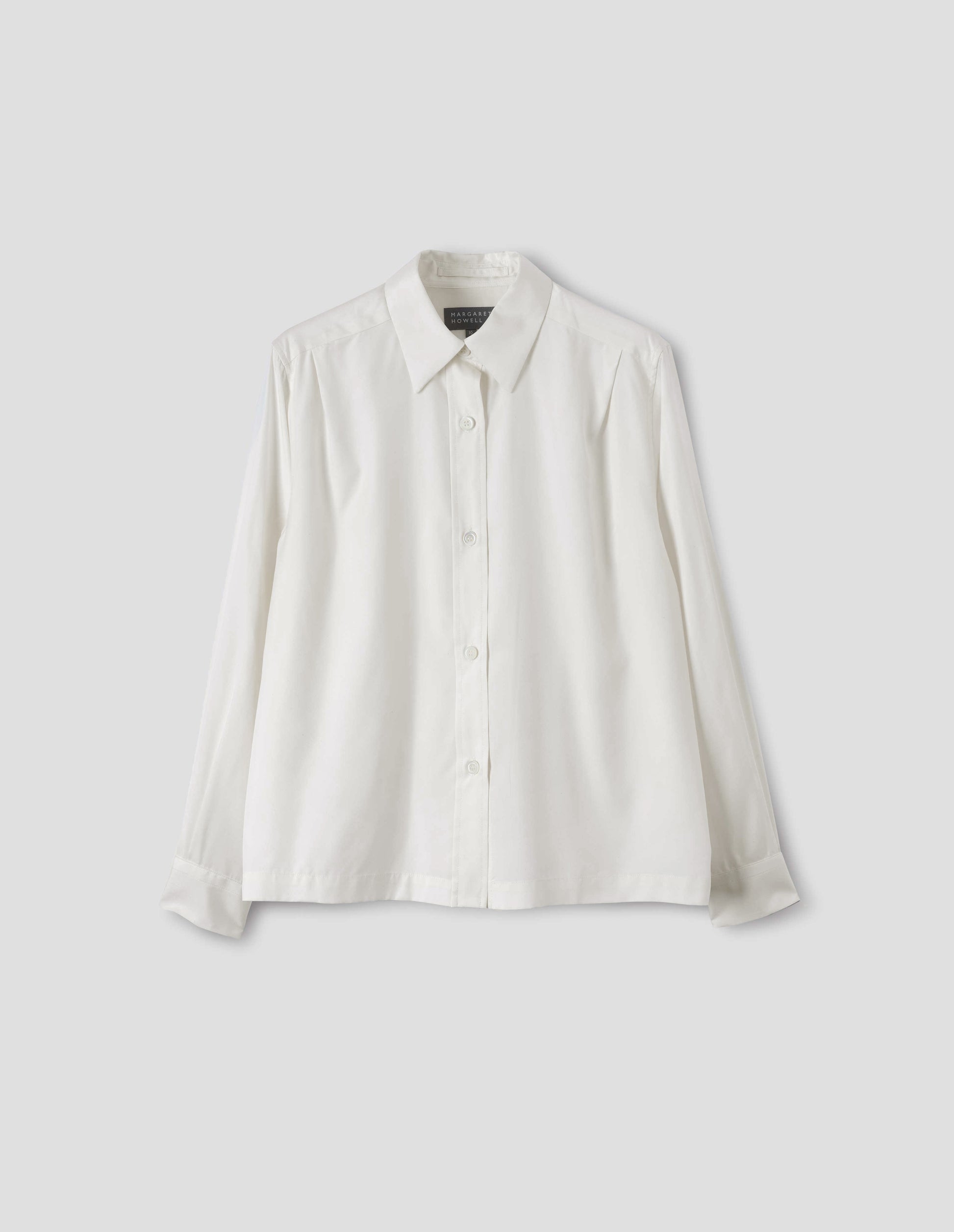 White silk shirt with mother of pearl buttons on placket and angled cuffs, narrow shoulder yoke with two pleats, and with vent split hem. Front flat lay view.