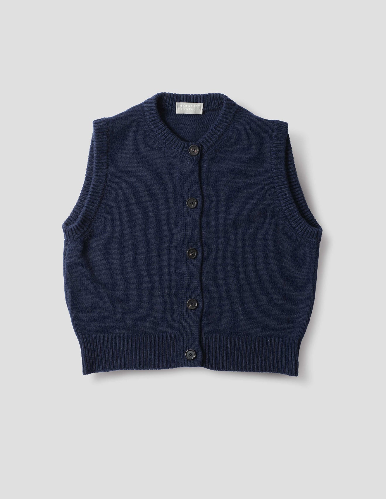 Dark blue cashmere merino knitted gilet with horn buttons on Milano stitch placket, rib detailing at neck, armholes and hem. Front flat lay view.
