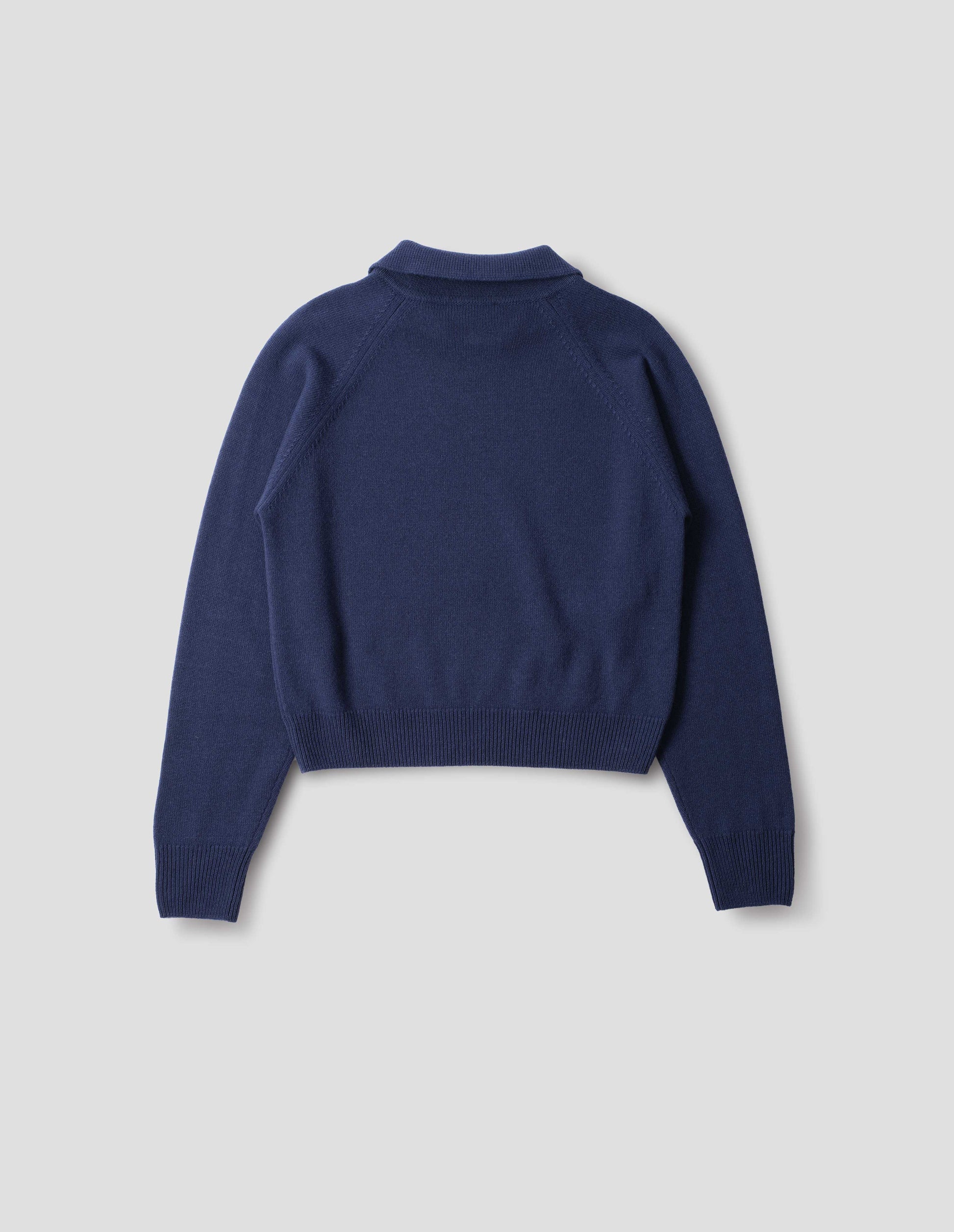 Dark blue merino jumper with collar, raglan sleeves, ribbed cuffs and hem. Back flat lay view.