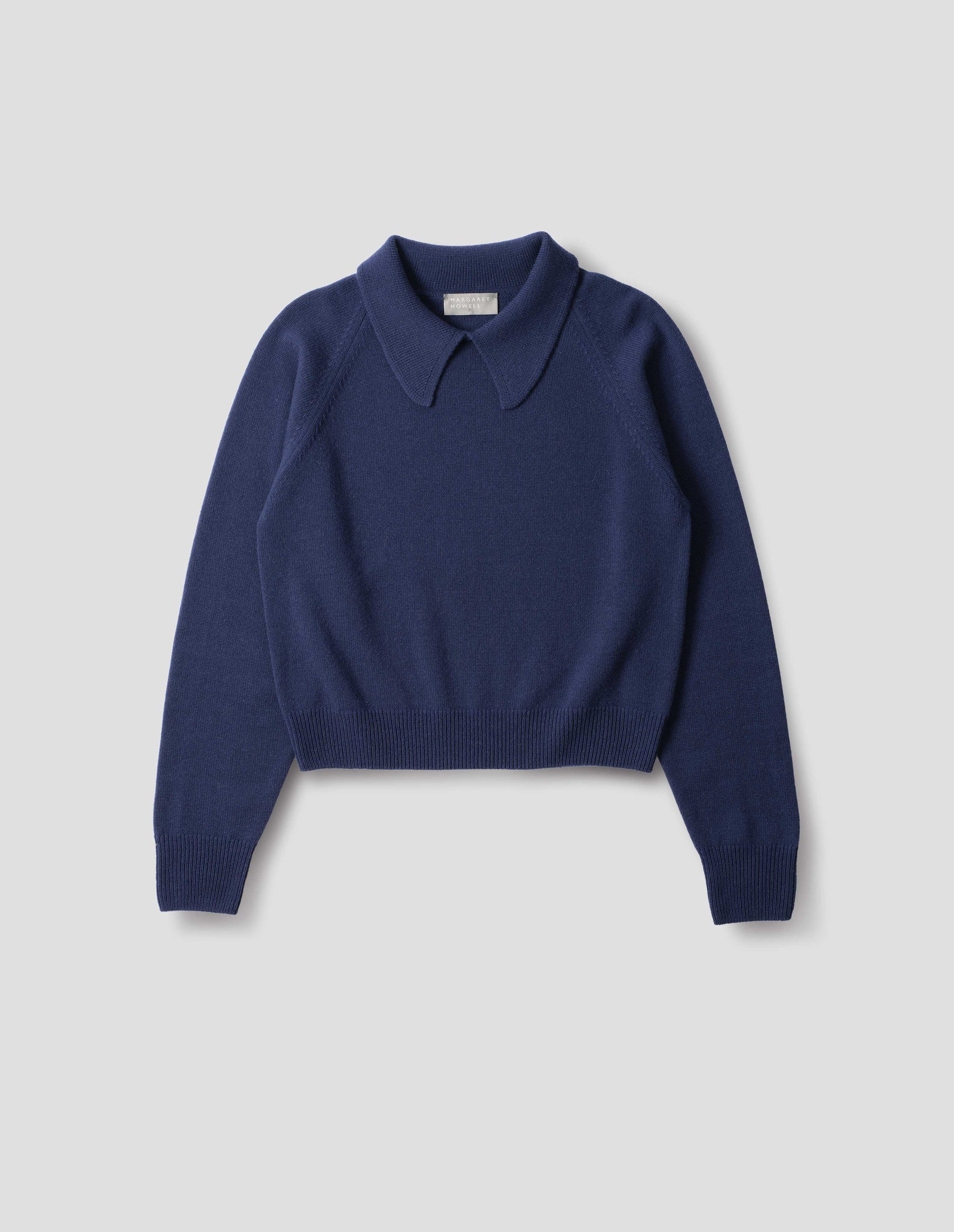 Dark blue merino jumper with exaggerated collar, raglan sleeves, ribbed cuffs and hem. Front flat lay view.