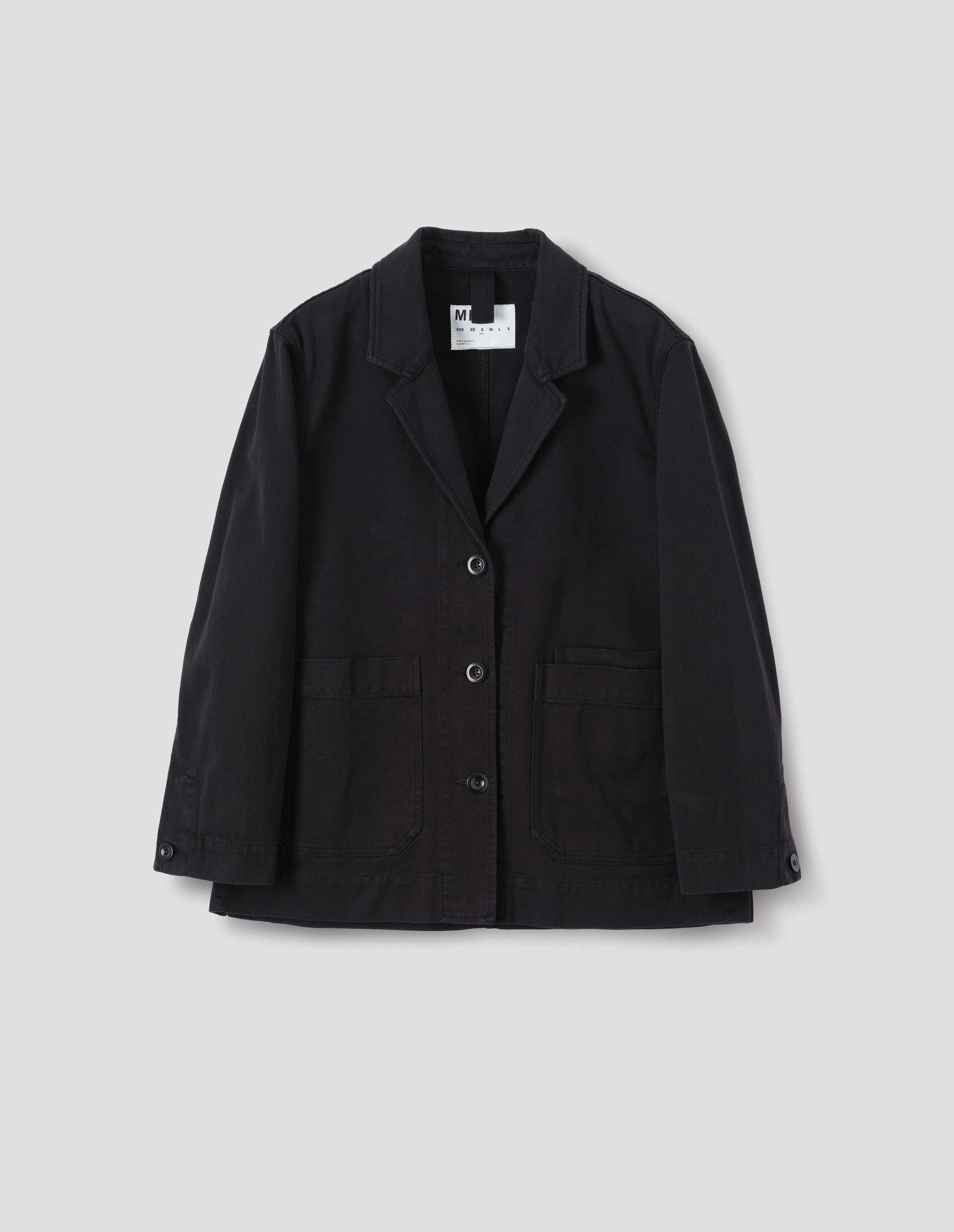 Black cotton blazer with a low breakpoint and three button closure, a wide placket, big front patch pocket with a double pocket detail and grown-on cuffs, front flat lay view.