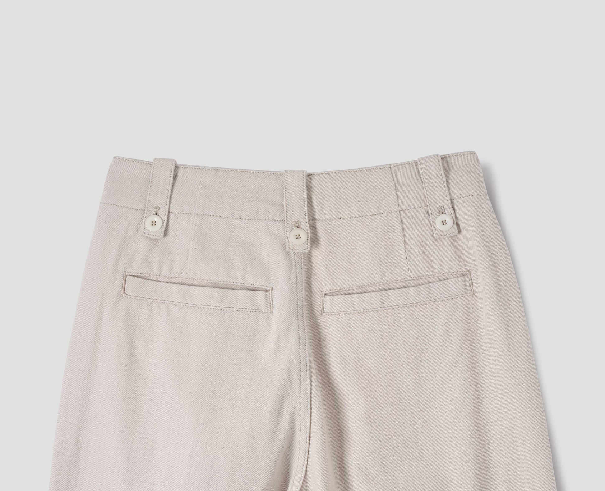 Off white trousers with grown-on waistband, button-fastening belt loops, and two back welt pockets. Back flat lay view.