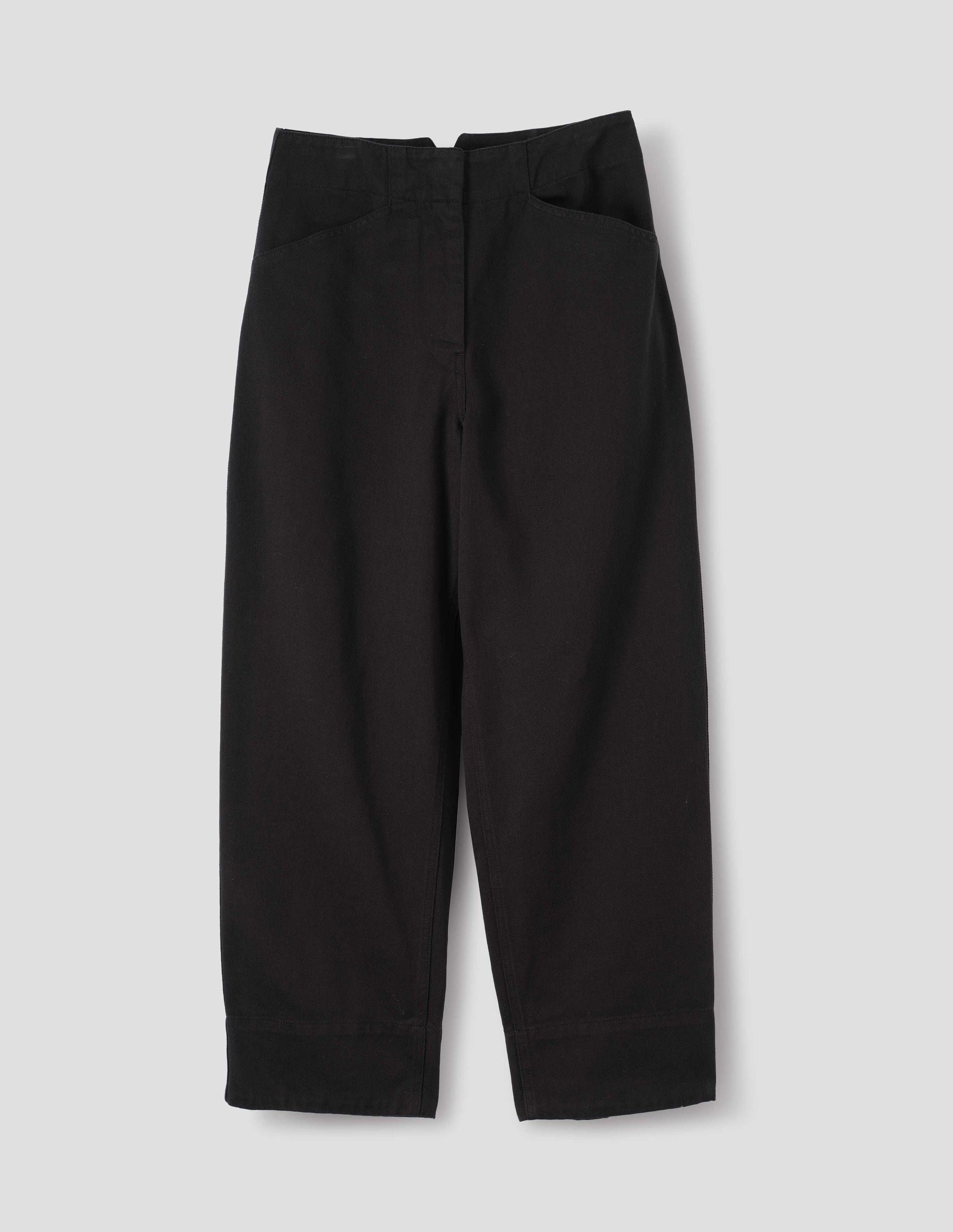 Black cotton drill straight leg trousers with a stitch-through waistband with a concealed double hook and bar fastening, frog pockets and deep stitch-through hem. Front flat lay view.