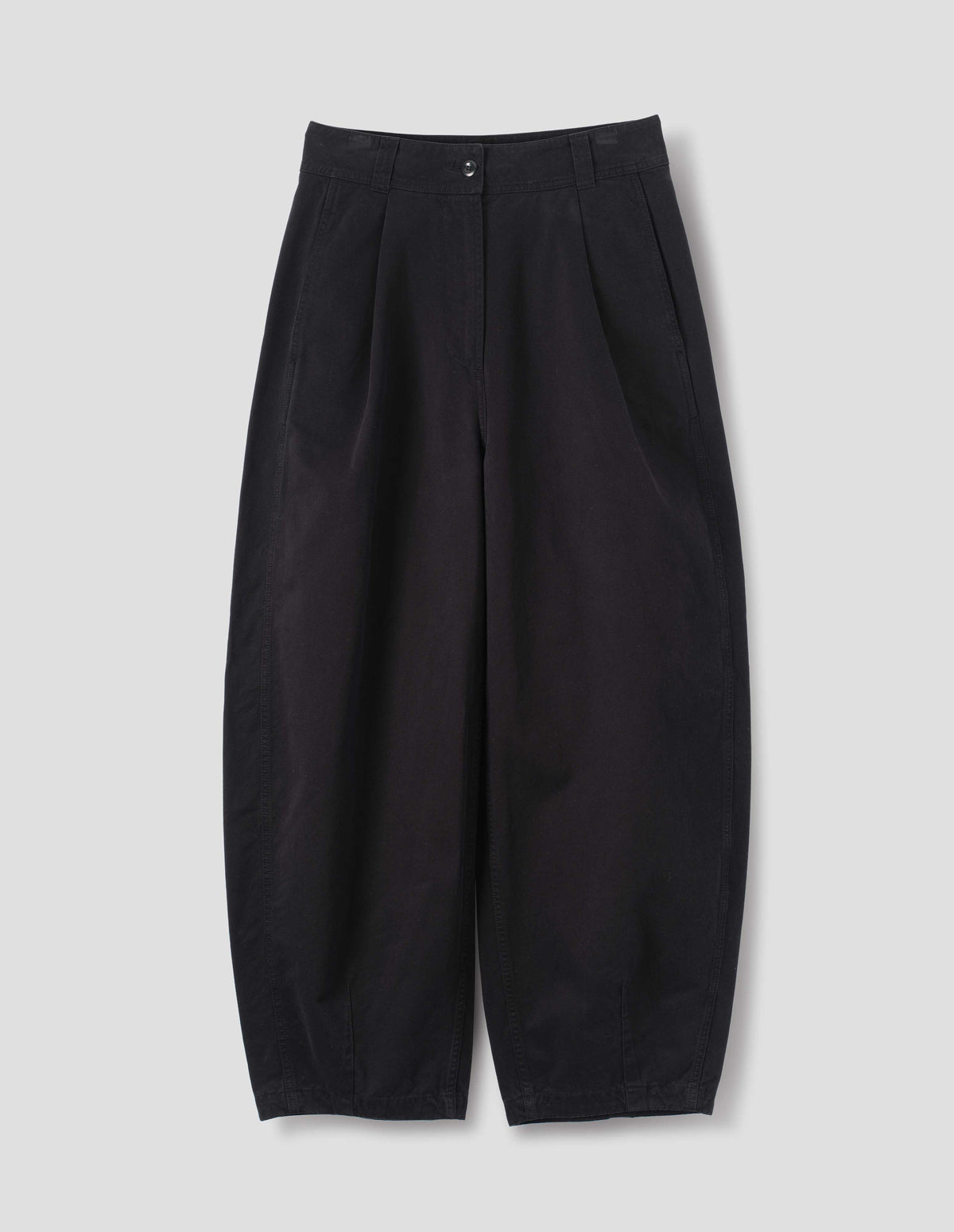 Black cotton trousers with a forward side seam and side seam pockets, deep single pleats at the front, darts at the hem, front flat lay view.