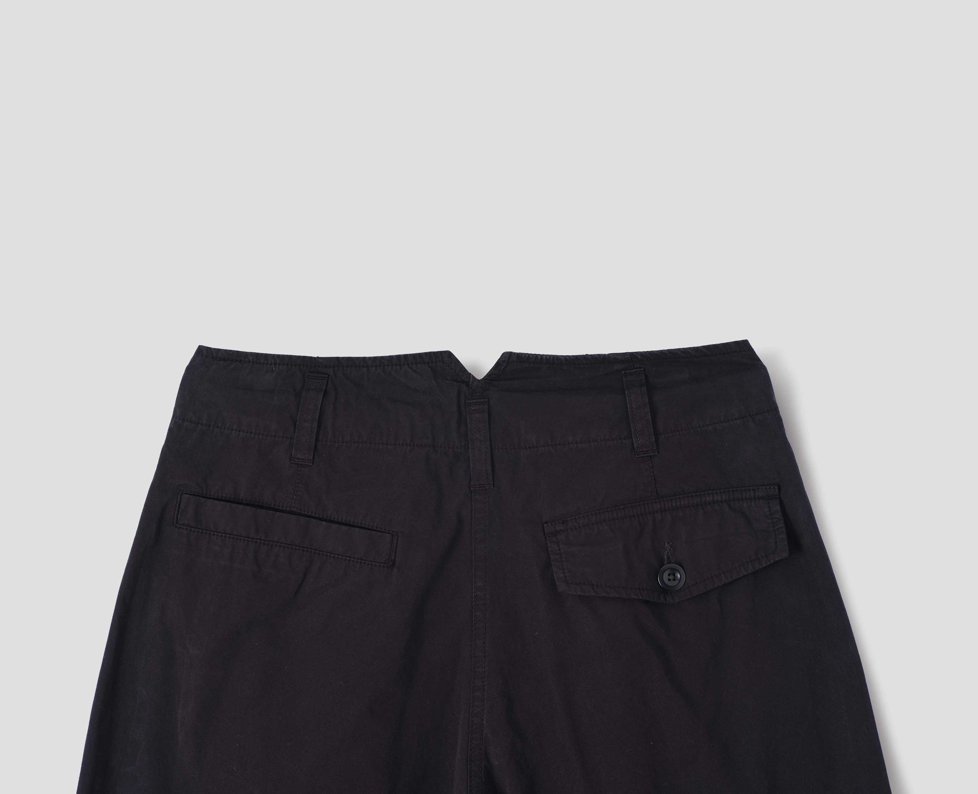 Black cotton trousers, with belt loops and V shape cutaway on waistband, one welt pocket and one button-fastening flap pocket, back flat lay view.