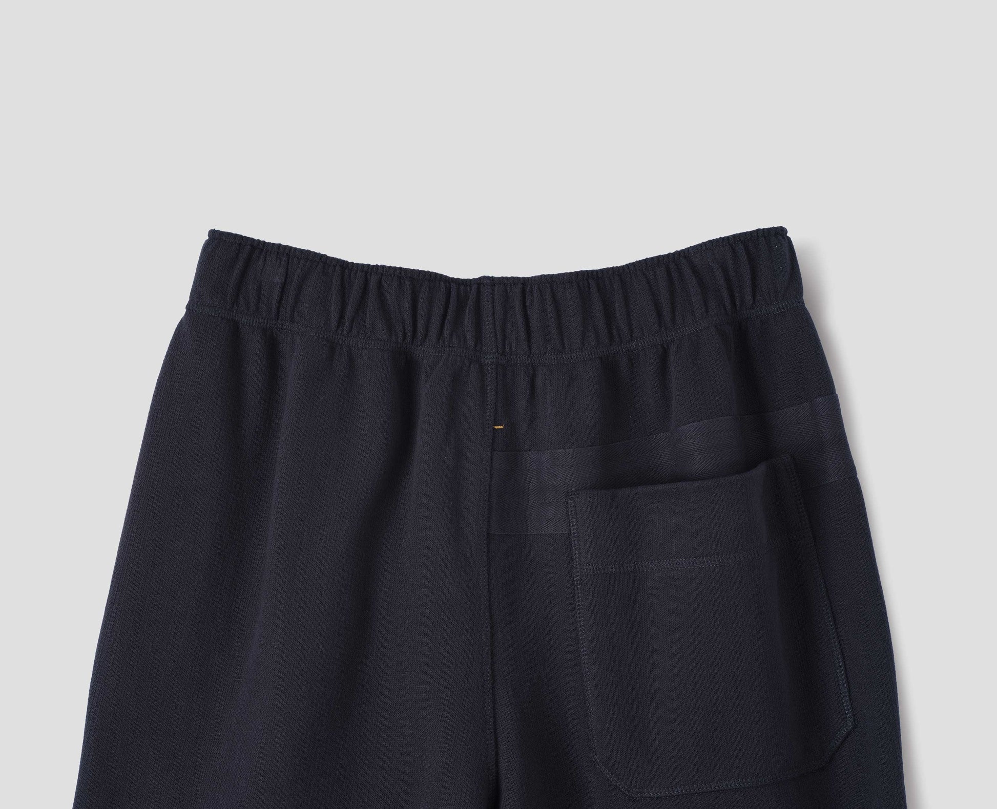 Dark navy lightweight jogger style trousers with back patch pocket and elasticated waistband, back flat lay view.