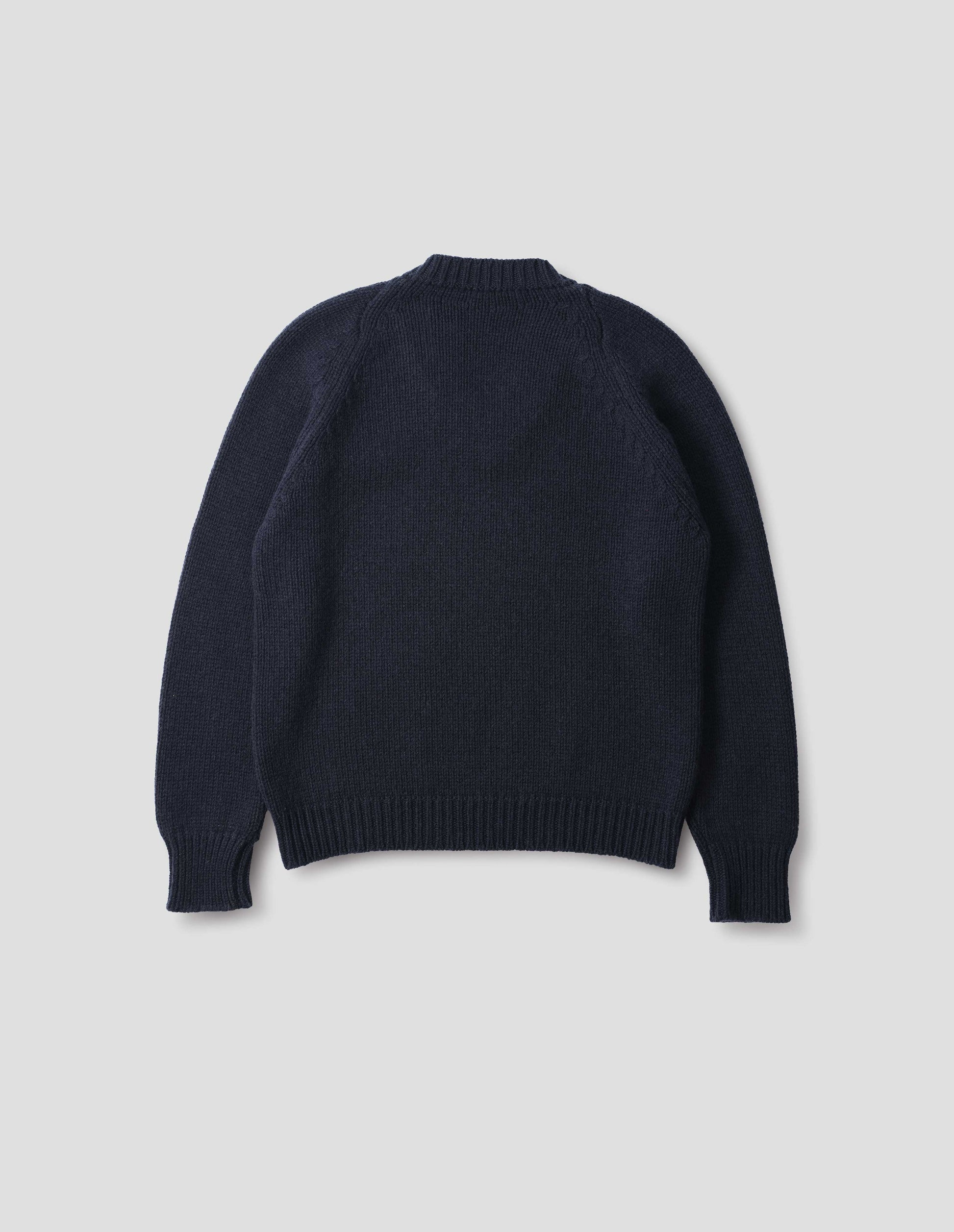 Dark blue cashmere wool jumper with raglan sleeve and fully fashioned arm hole, ribbed neck, cuffs and hem. Back flat lay view.