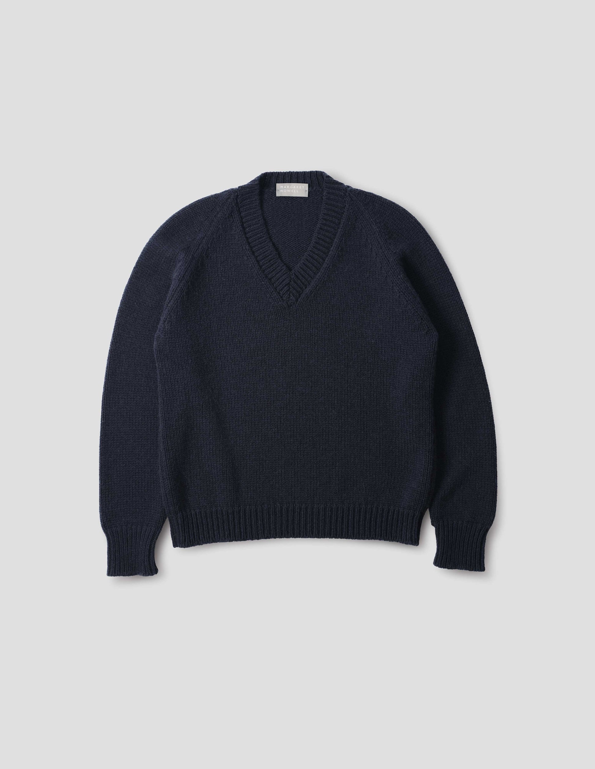 Dark blue cashmere wool jumper with V neck, raglan sleeve and fully fashioned arm hole, ribbed neck, cuffs and hem. Front flat lay view.