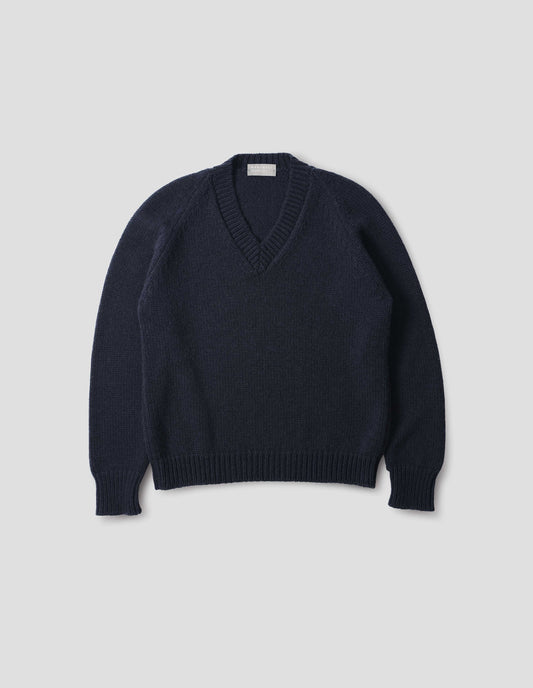 Dark blue cashmere wool jumper with V neck, raglan sleeve and fully fashioned arm hole, ribbed neck, cuffs and hem. Front flat lay view.