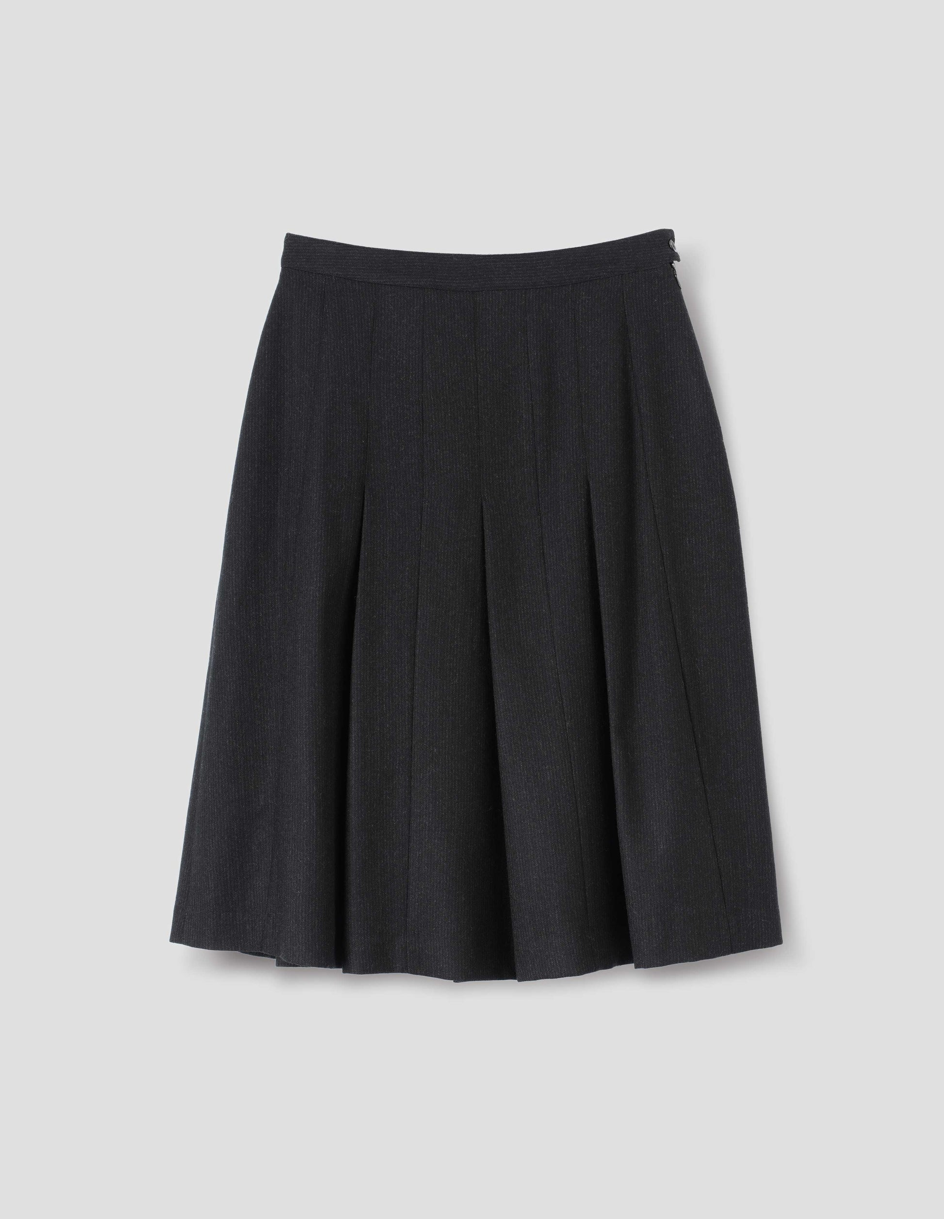 Black wool skirt with dark grey stripes, pleats, narrow horn button-through waistband and side zip fly. Front flat lay view.