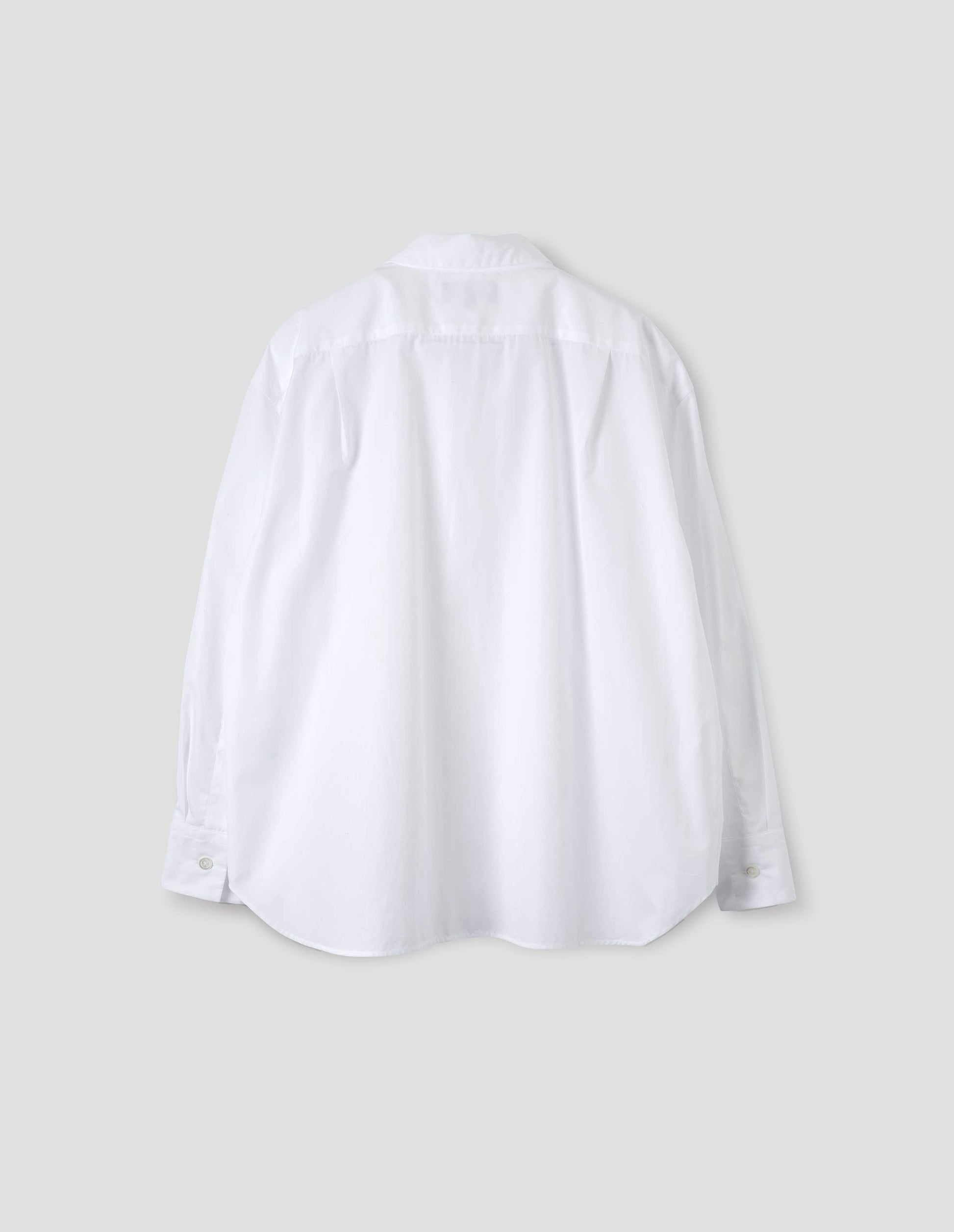 White cotton shirt with back yoke and two small pleats, mother of pearl buttons on cuffs, and curved hem. Back flat lay view.