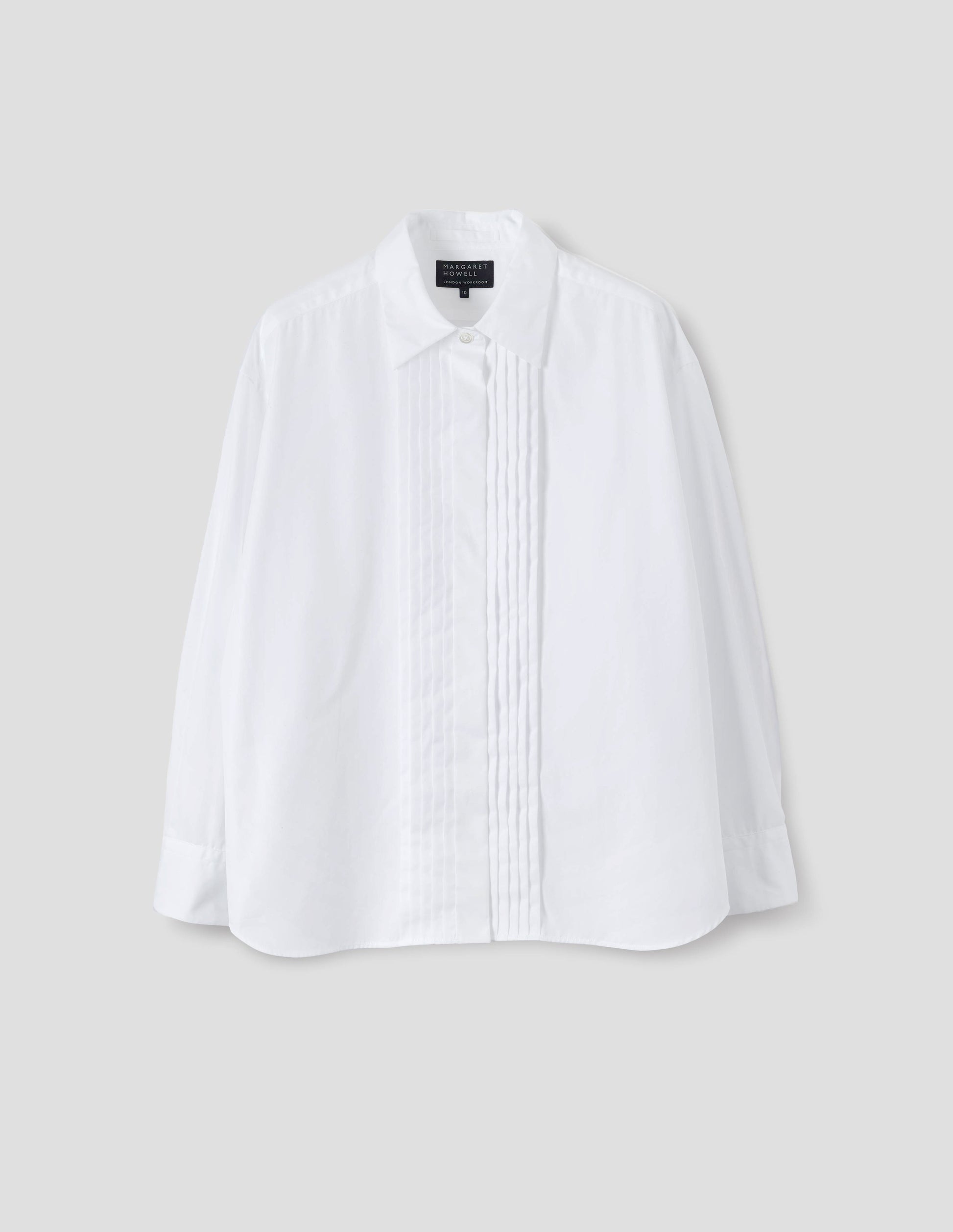 White cotton shirt with mother of pearl button closure, concealed placket and pin tuck detailing at front, and with curved hem. Front flat lay view.