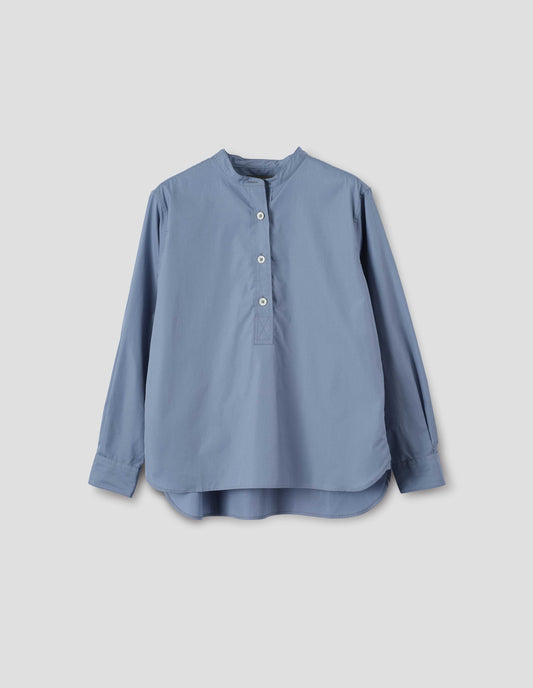 Blue cotton poplin collarless pull on shirt with mother of pearl buttons on placket with box stitch detailing and curved stepped hem. Front flat lay view.