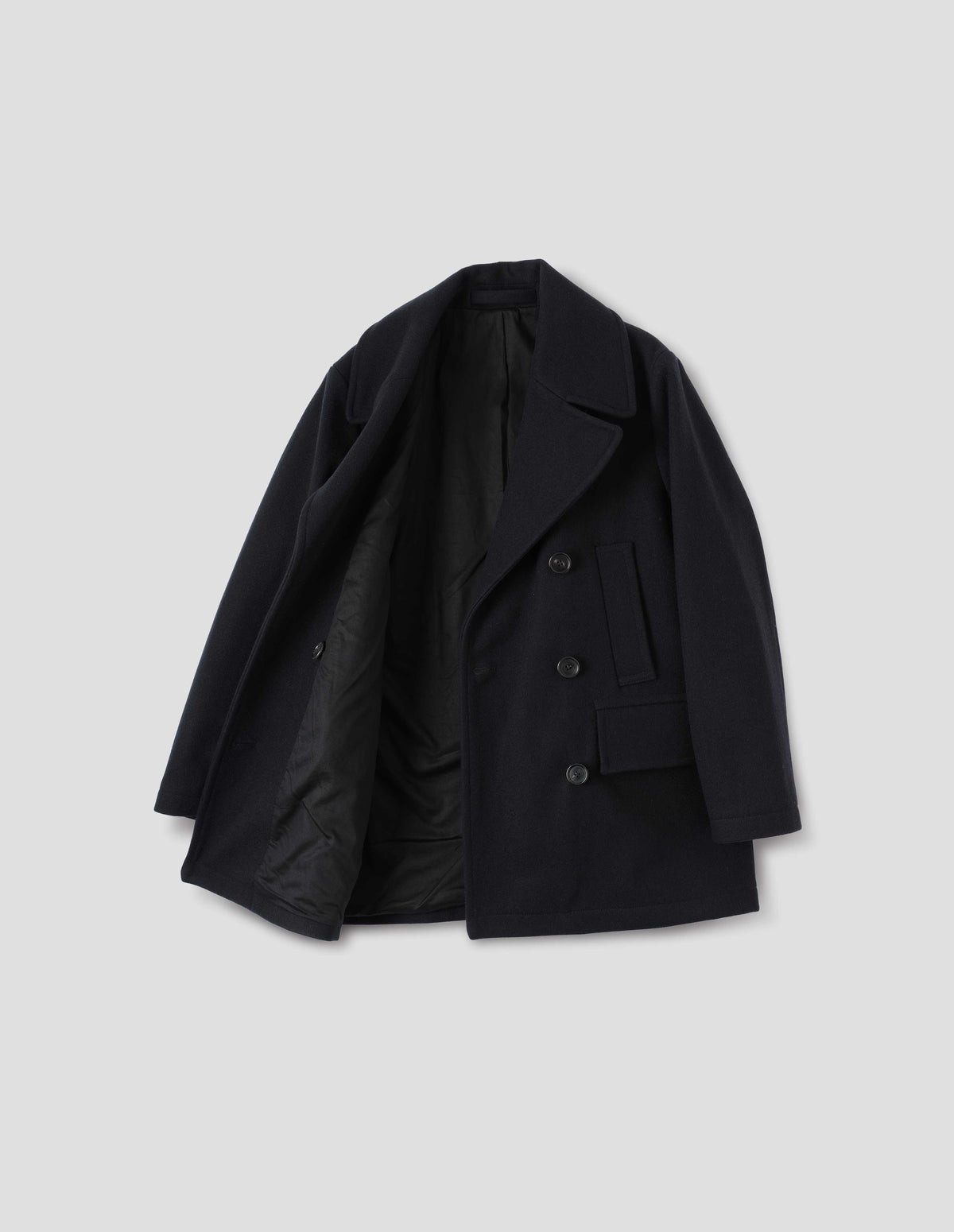 Dark blue cotton lined wool coat with large collar and revere, horn buttons, high-set single welt pockets and large flap pockets. Open flat lay view.