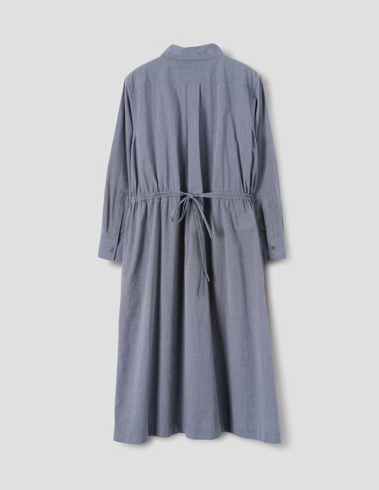Blue cotton dress with collar, pleat on narrow yoke on back, shirt sleeves with mother of pearl buttons on cuffs, externally applied channel at waist with double tie. Back flat lay view.