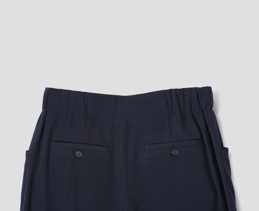 Dark blue wool trousers with elasticated waistband and horn button-through jet back pockets. Back flat lay view.