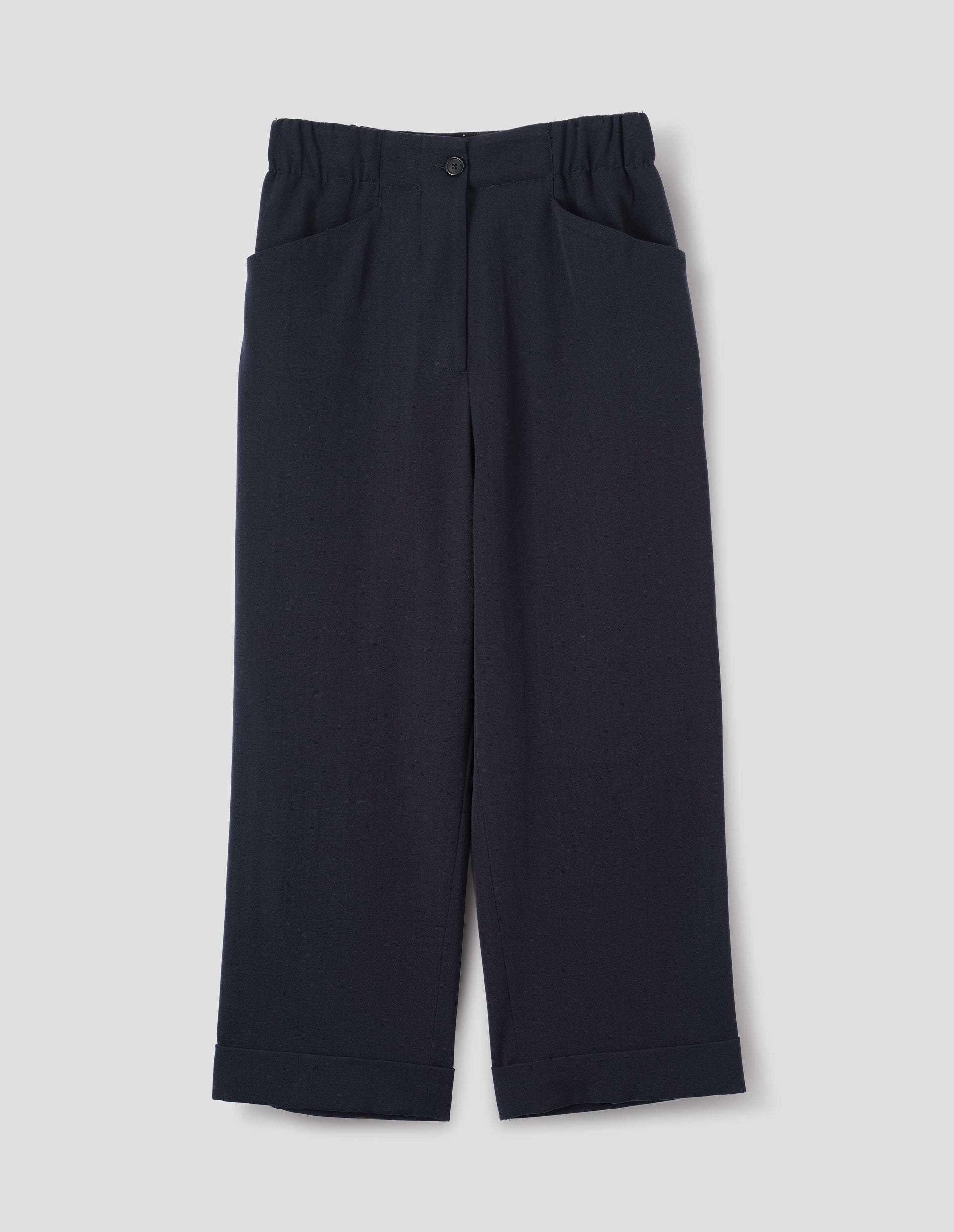 Dark blue wool trousers with zip fly with horn button fastening on elasticated waistband, frog pockets and stitch-down turn-up hem. Front flat lay view.