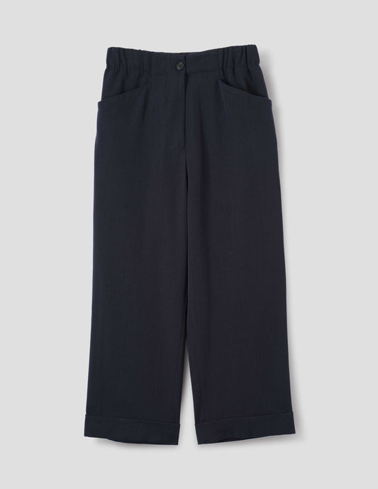 Dark blue wool trousers with zip fly with horn button fastening on elasticated waistband, frog pockets and stitch-down turn-up hem. Front flat lay view.