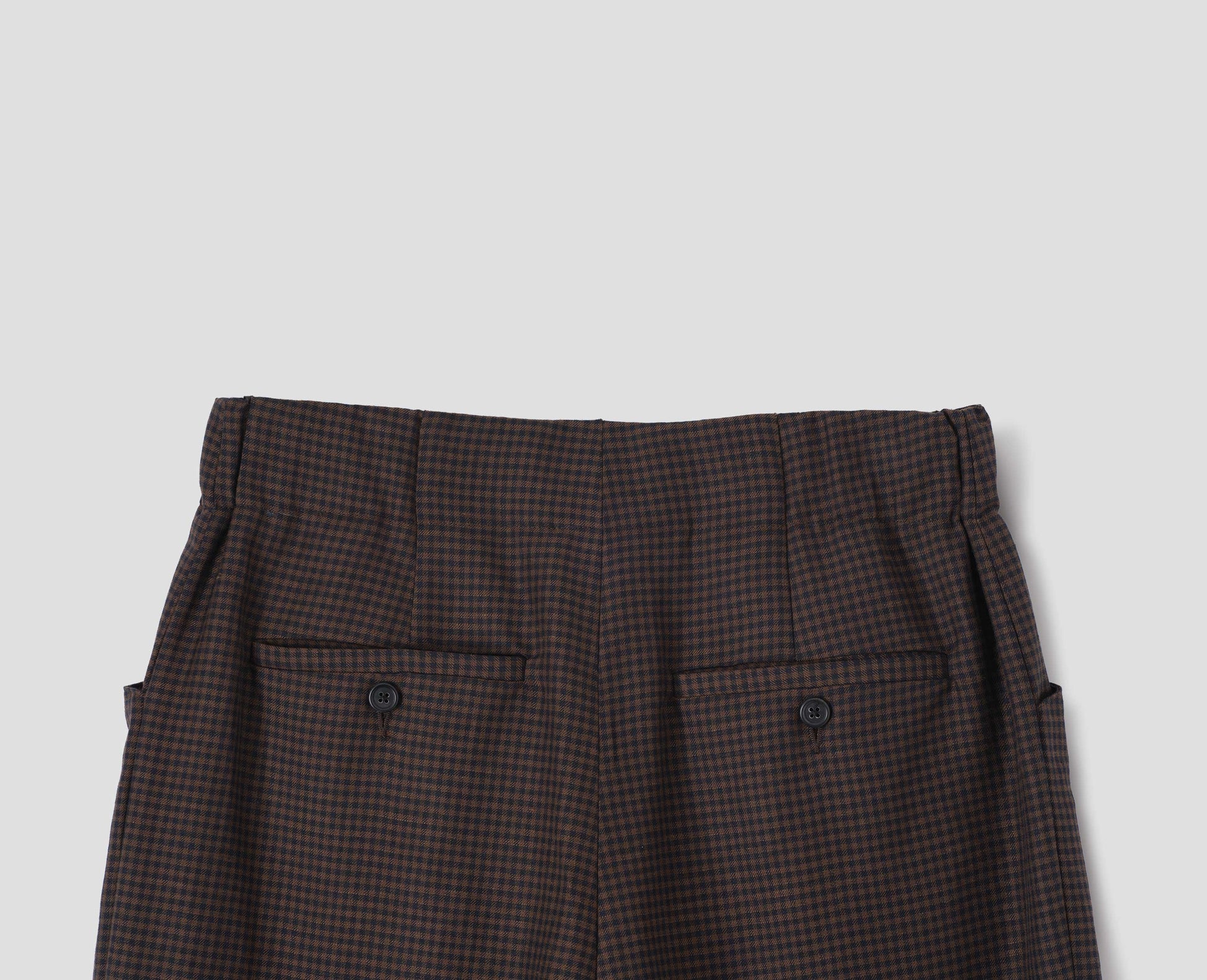 Dark blue and dark brown linen wool gingham trousers with elasticated waistband and horn button-through jet back pockets. Back flat lay view.